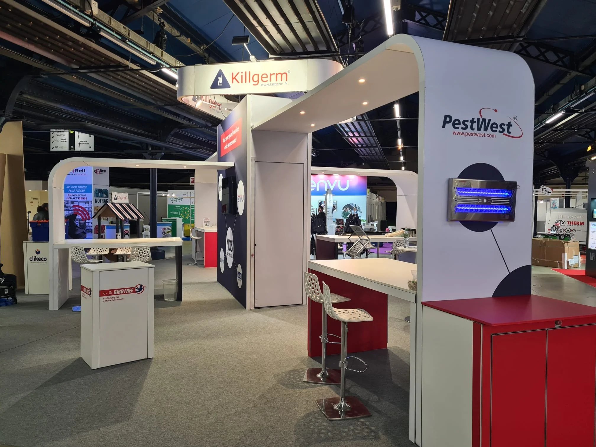 Island Trade show booth, featuring a white counter with a red top, white chairs, and equipment displays in a large exhibition hall.