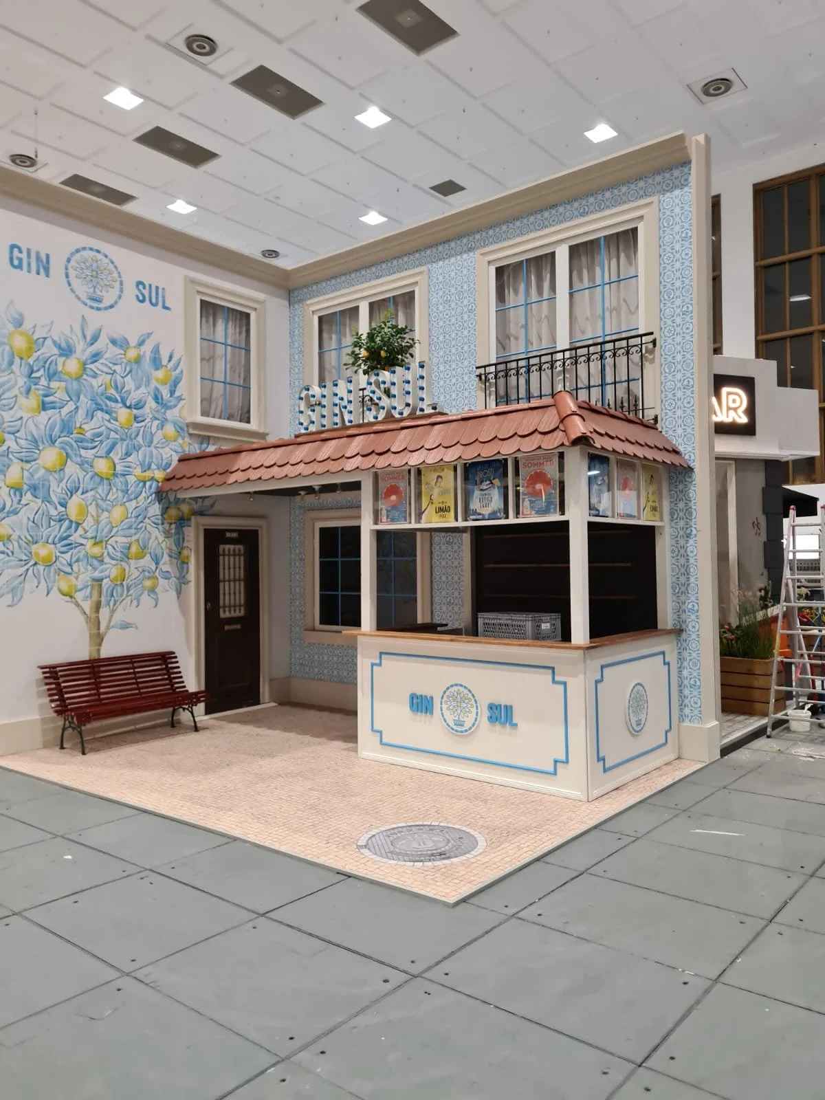 A small e styled as a traditional German or Austrian house with decorative blue and white patterns, a red-tiled roof.  The kiosk  a counter and a small seating area with a bench and a painted tree on the wall.