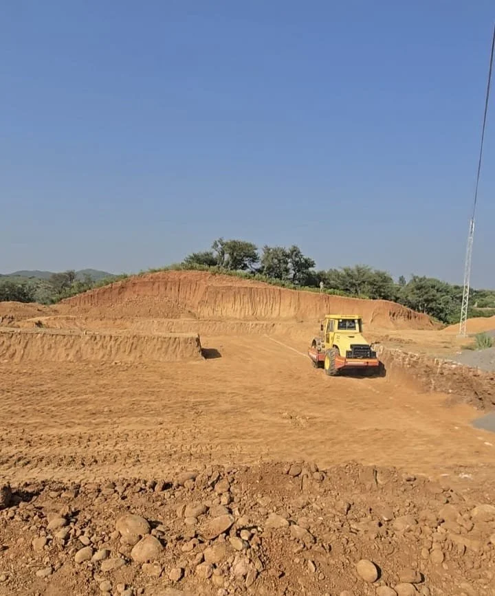 A yellow bulldozer working on a dirt construction site with mounds of earth and a clear blue sky.