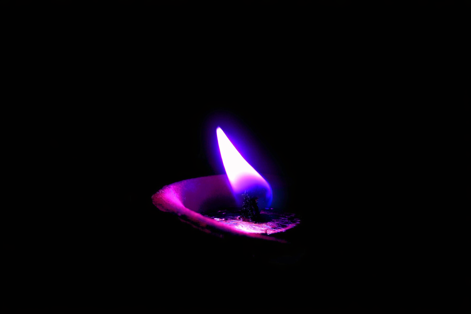 Close-up of a purple and white flame burning from a candle burning in darkness.