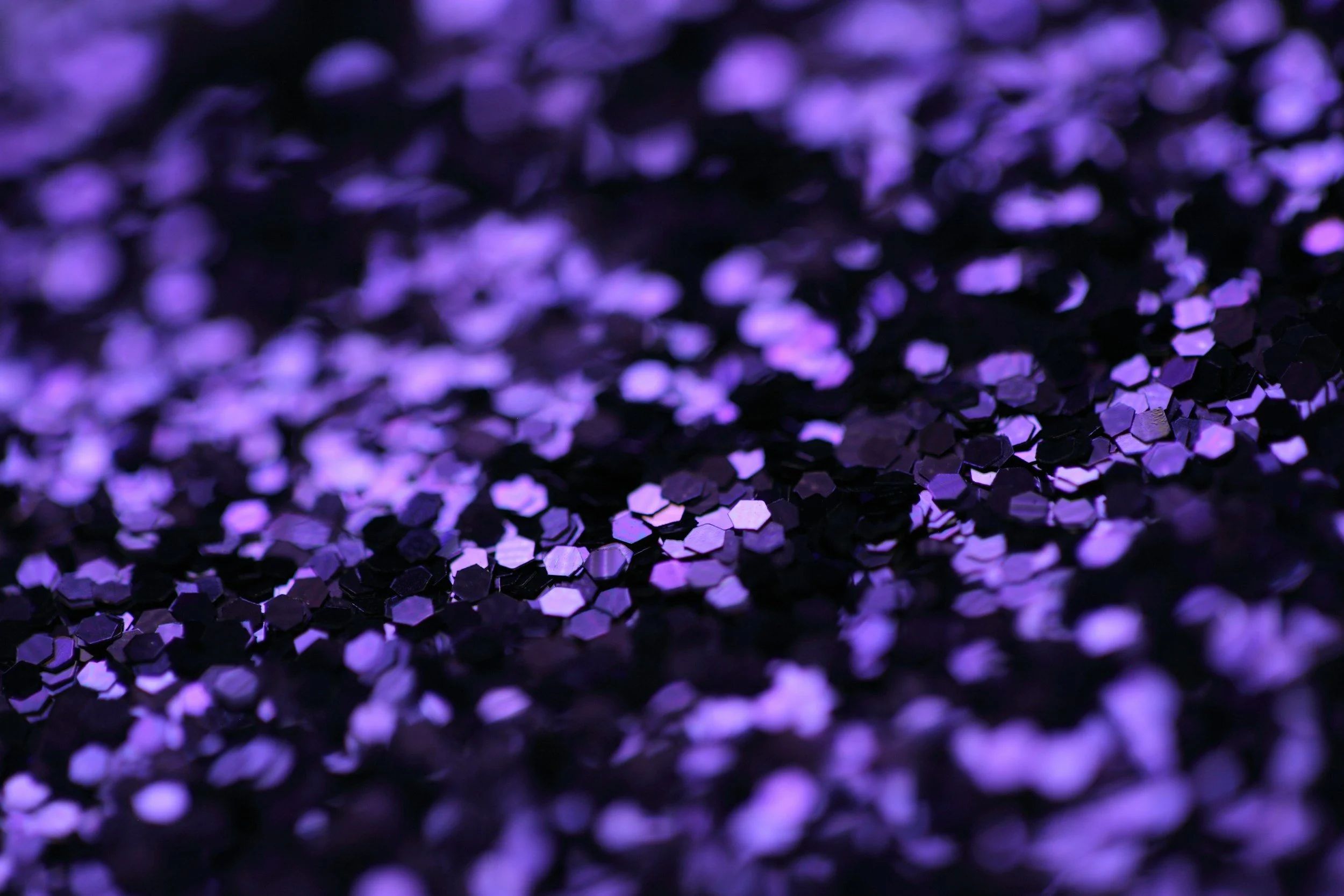 Close-up of purple glitter particles on a surface, reflecting light and creating a shimmering effect.