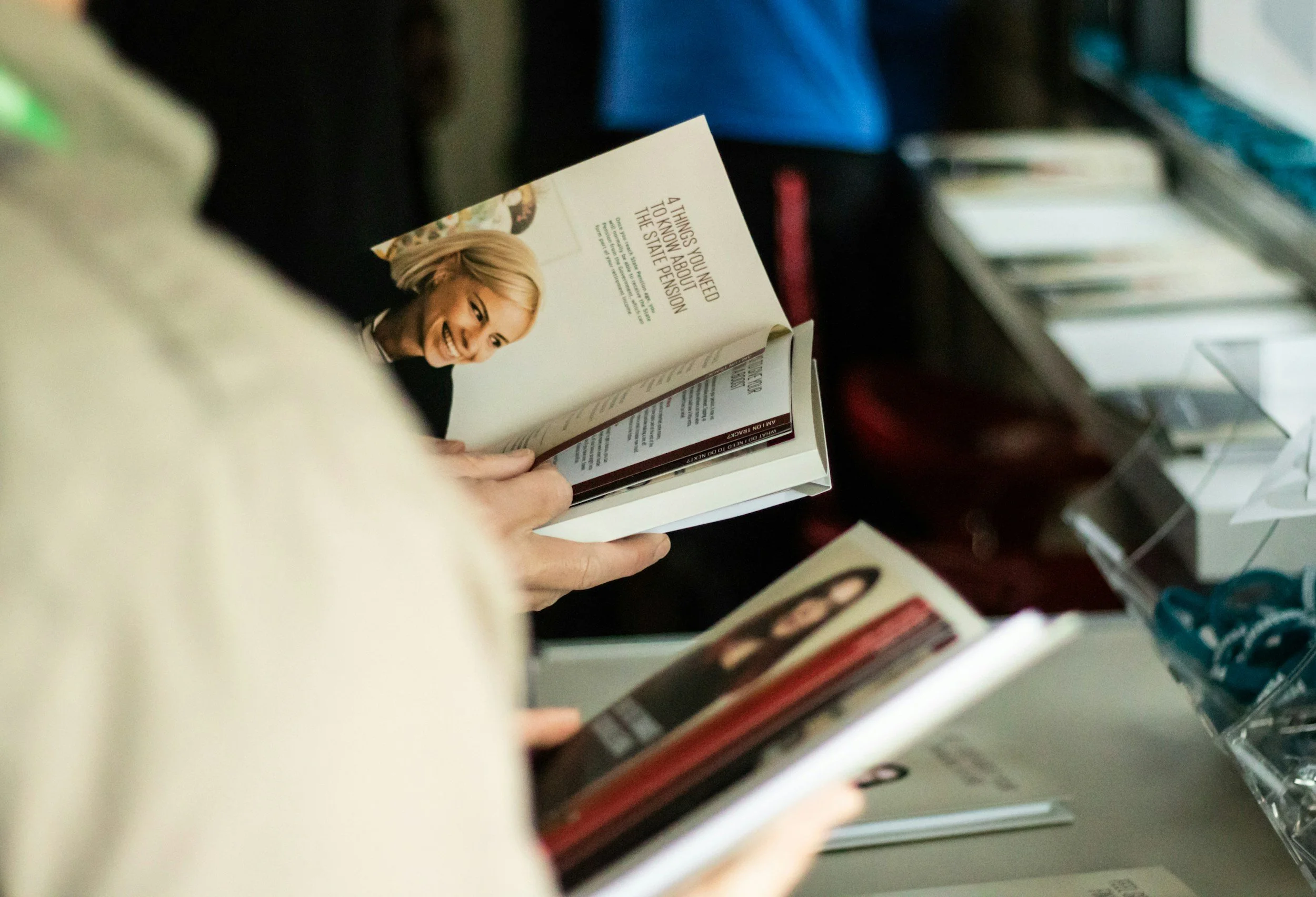 People browsing books at a store, with a focus on a woman holding a book with a woman's picture on the page.