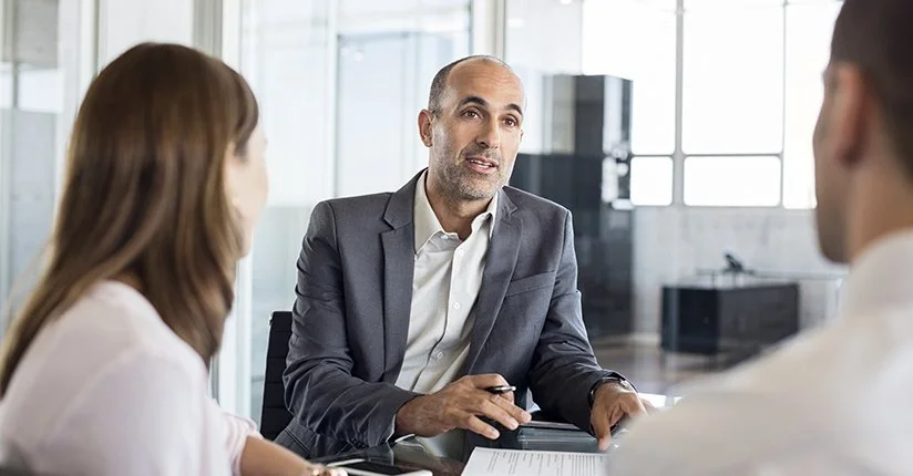 Man in business suit speaking during a meeting with two colleagues in a modern office.