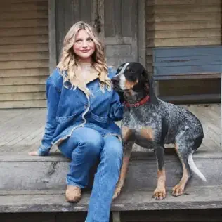 A woman sitting on wooden steps with a dog beside her, both looking at each other.