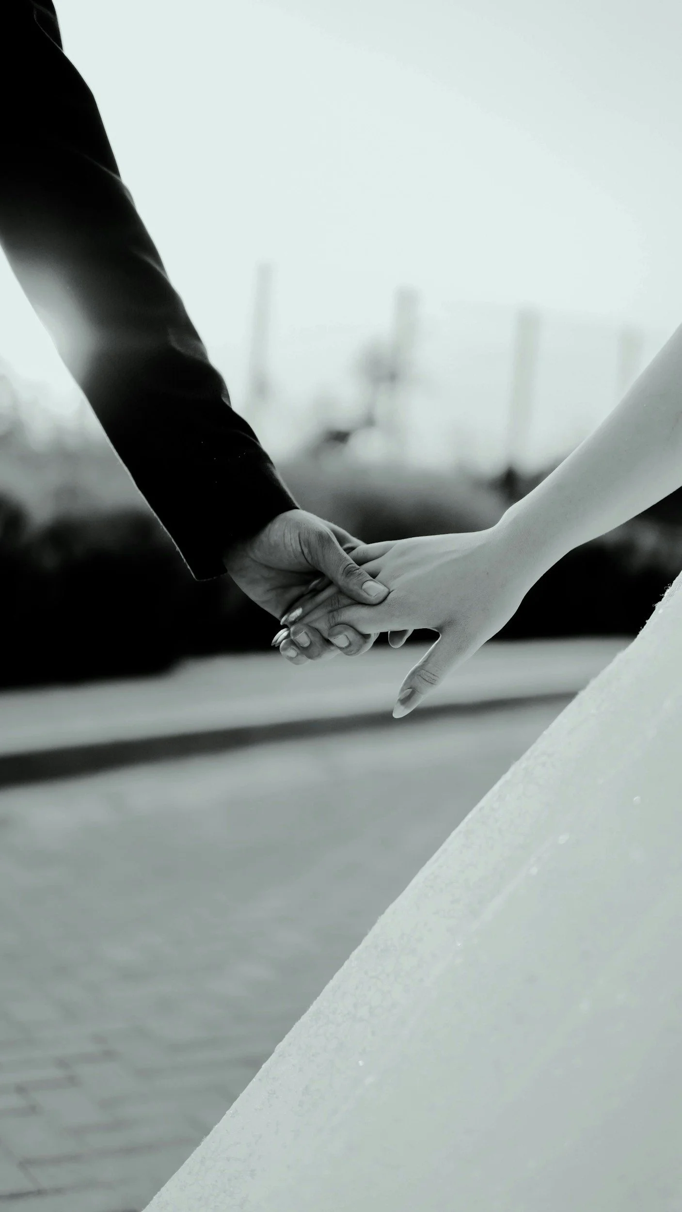 Close-up of two people holding hands, supported on a sloped concrete surface with a blurred cityscape background.