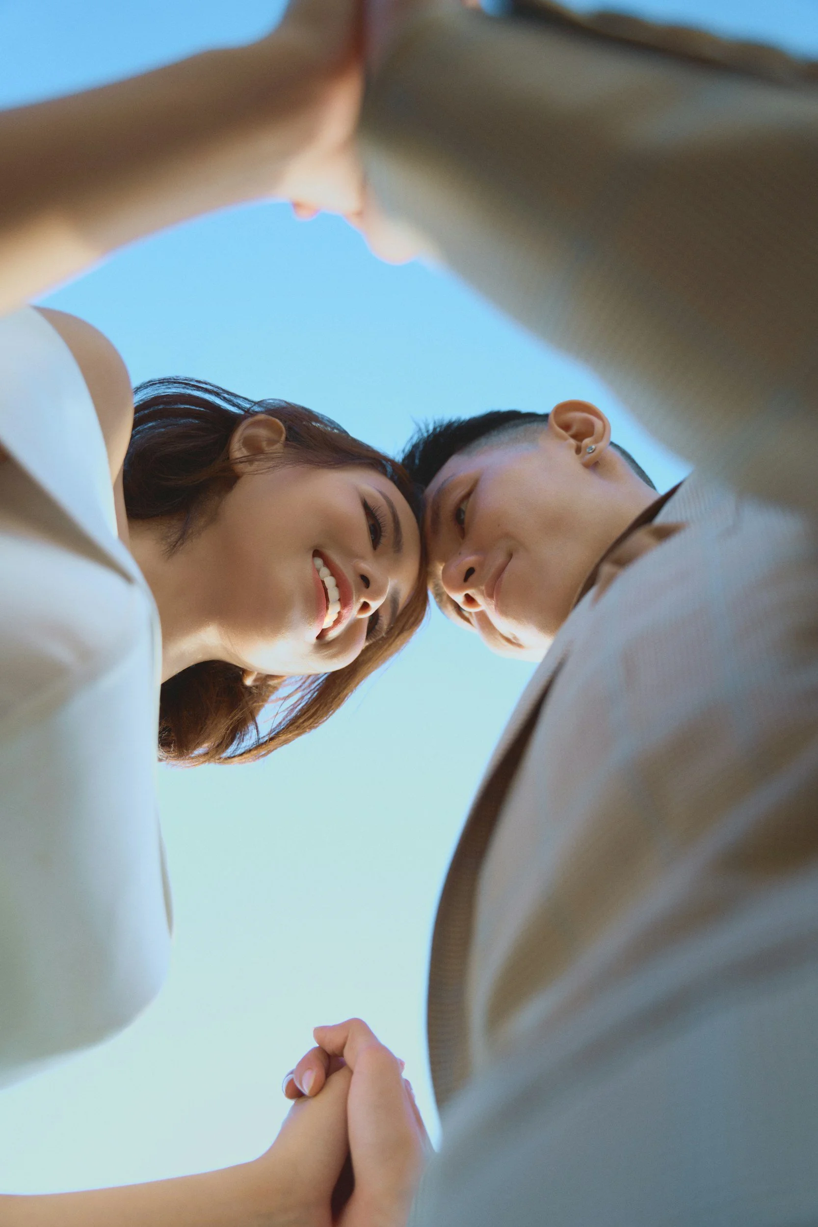 Two people holding hands in a gesture of unity, viewed from below against a blue sky background.