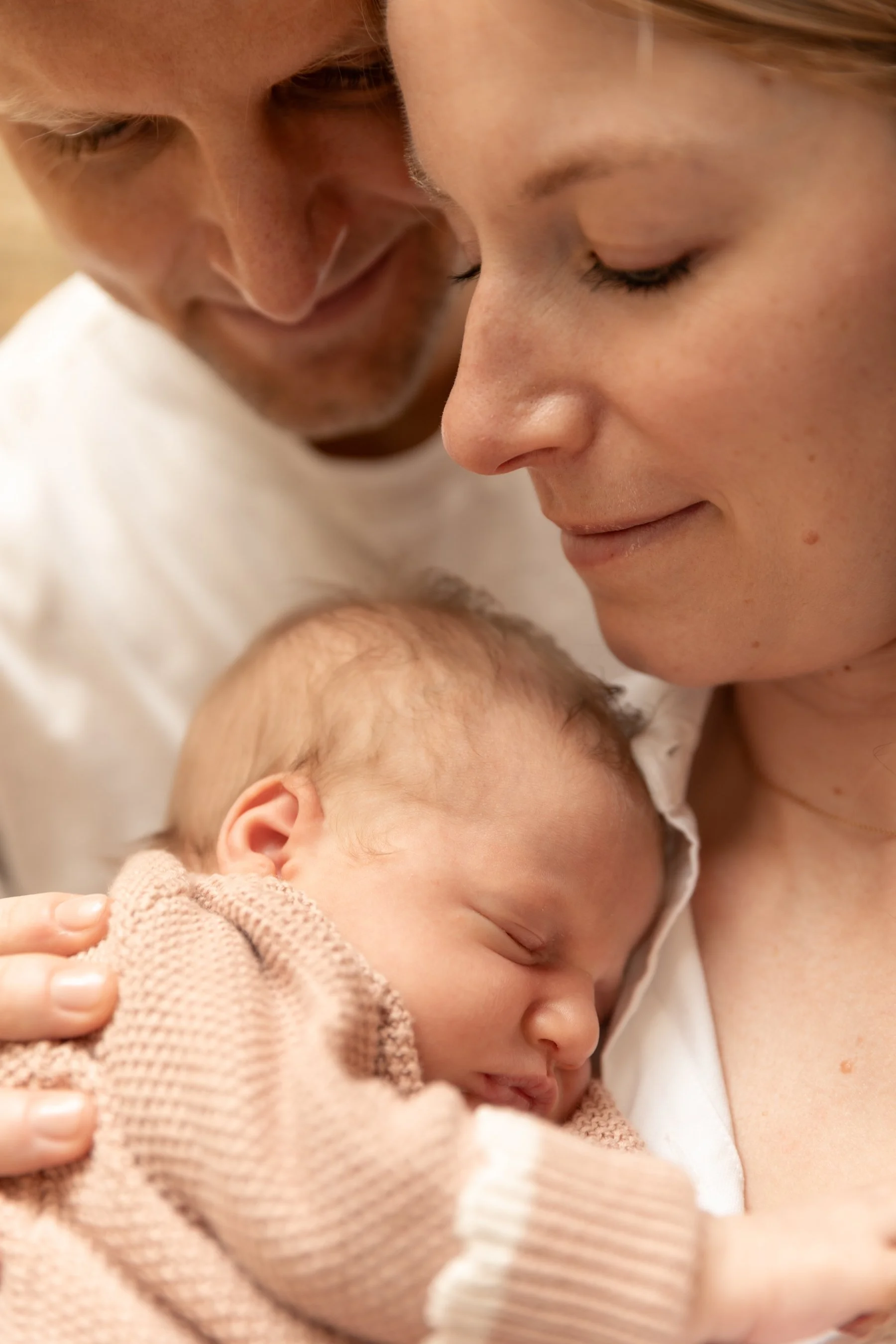 A young couple cradle their newborn baby I their arms during a relaxed shoot at home in Wandsworth