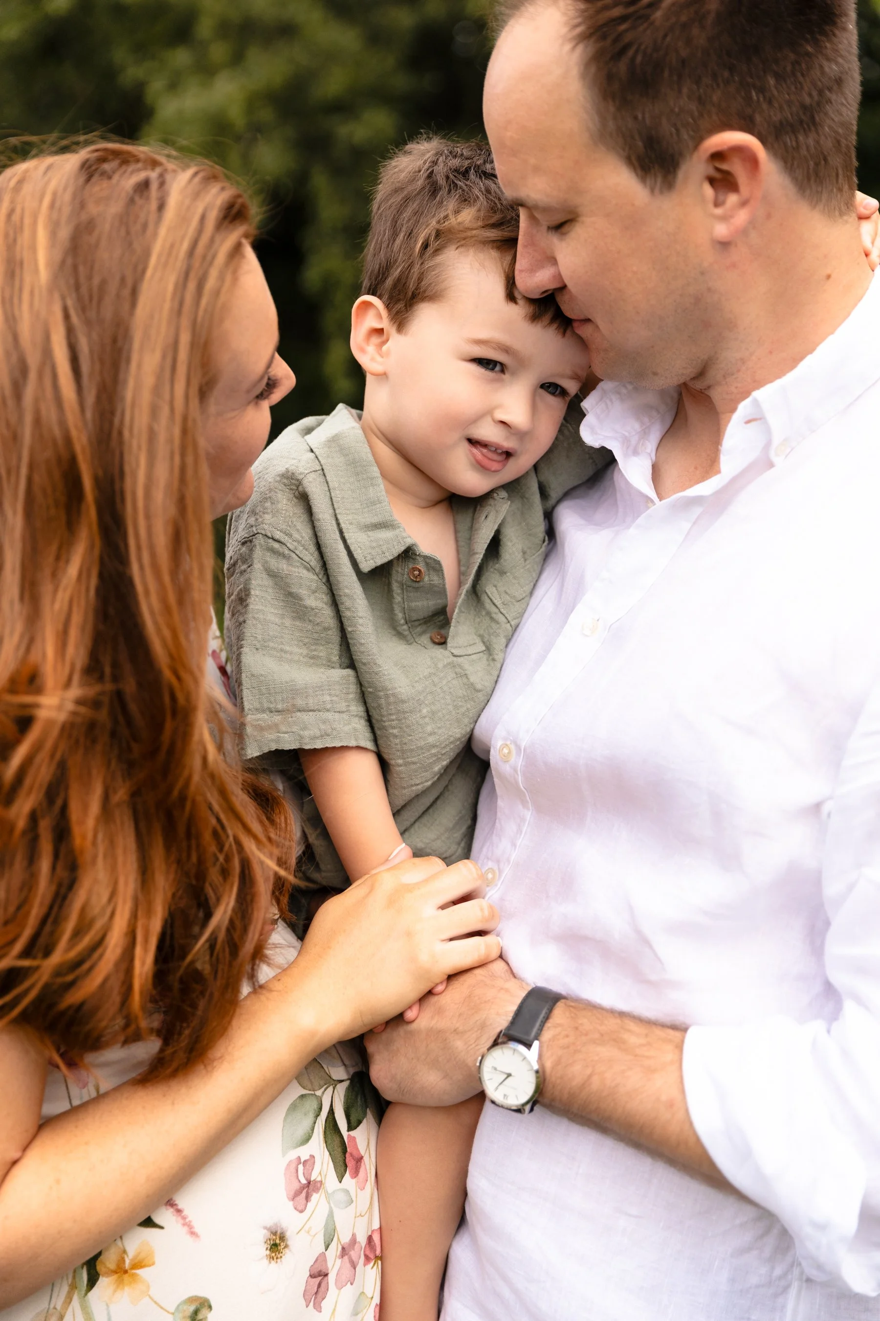 A pregnant couple cuddle their son lovingly between them at an outdoor maternity photoshoot in Earlsfield