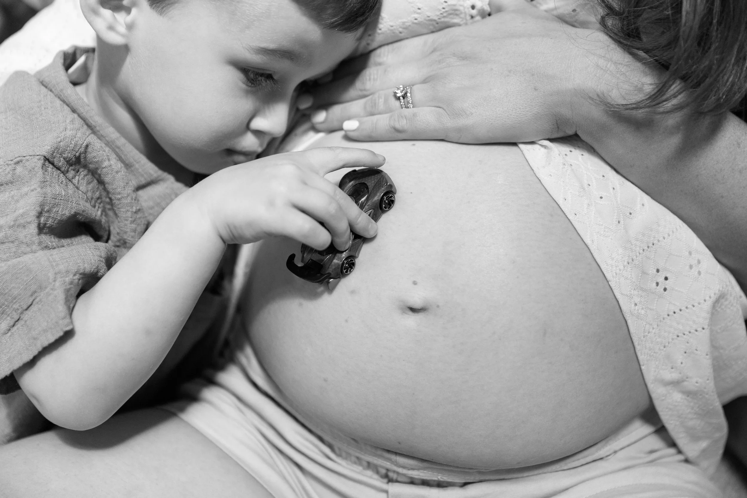 a black and white shot of a toddler racing his toy car over his pregnant mother's bump at a maternity shoot in Wandsworth 