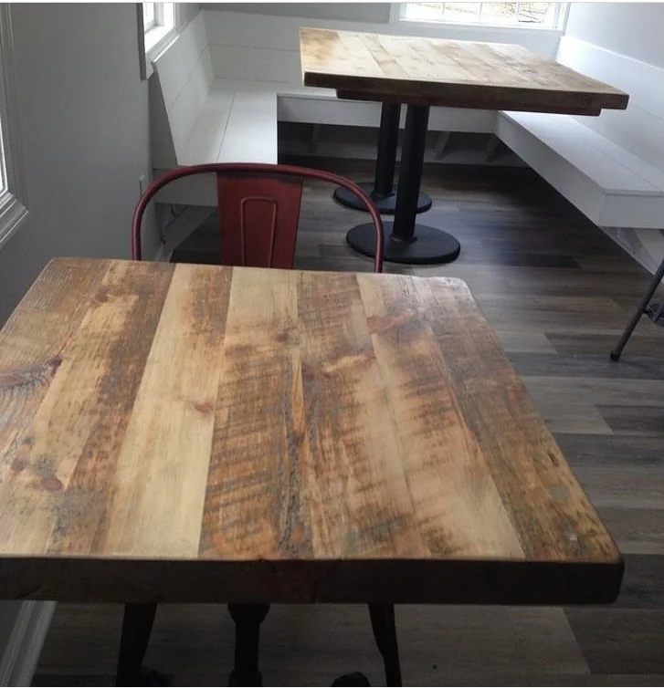 Two wooden tables in a room with hardwood floors and white walls, one in the foreground and one in the background, with a red metal chair near the foreground table.