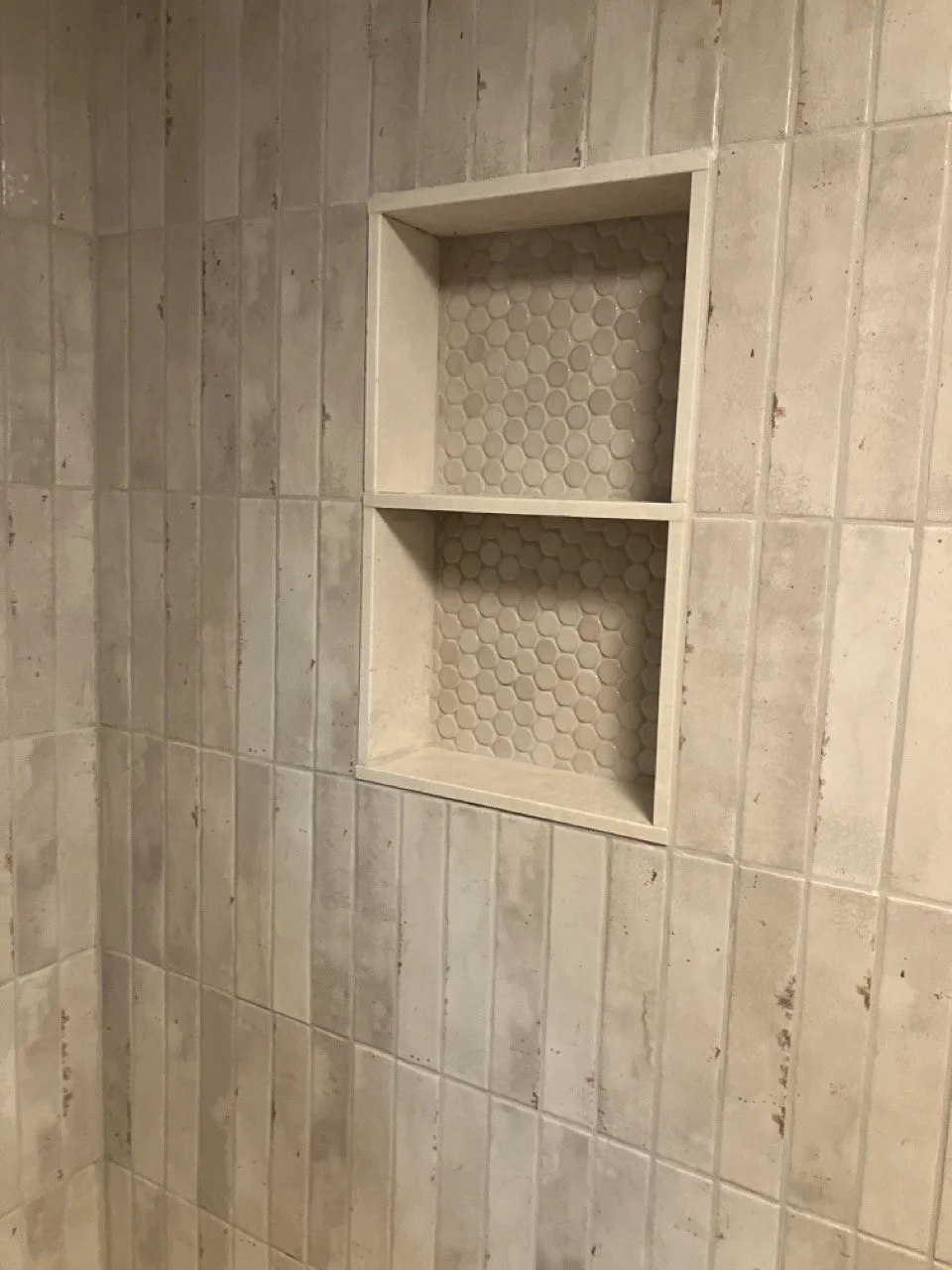 A shower wall with beige tiles and a built-in niche with honeycomb-patterned tiles.