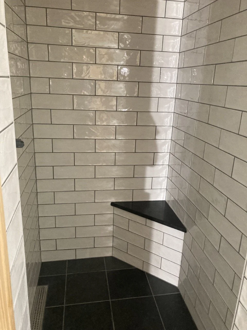 A corner shower with white subway tiles and a black corner shelf with a matte finish.