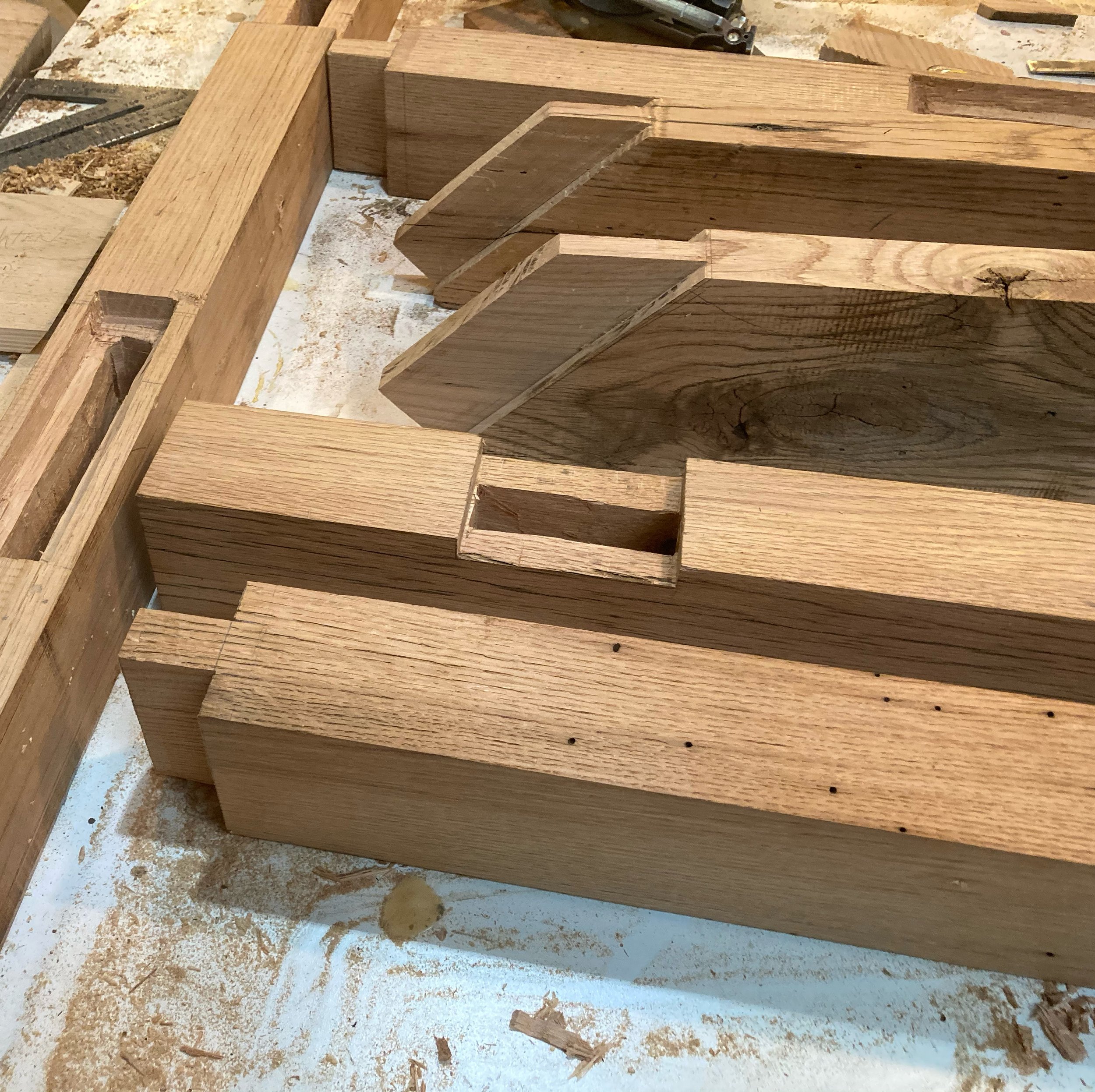 Wooden furniture parts assembled with some screw holes visible, on a workbench with shavings and debris around.
