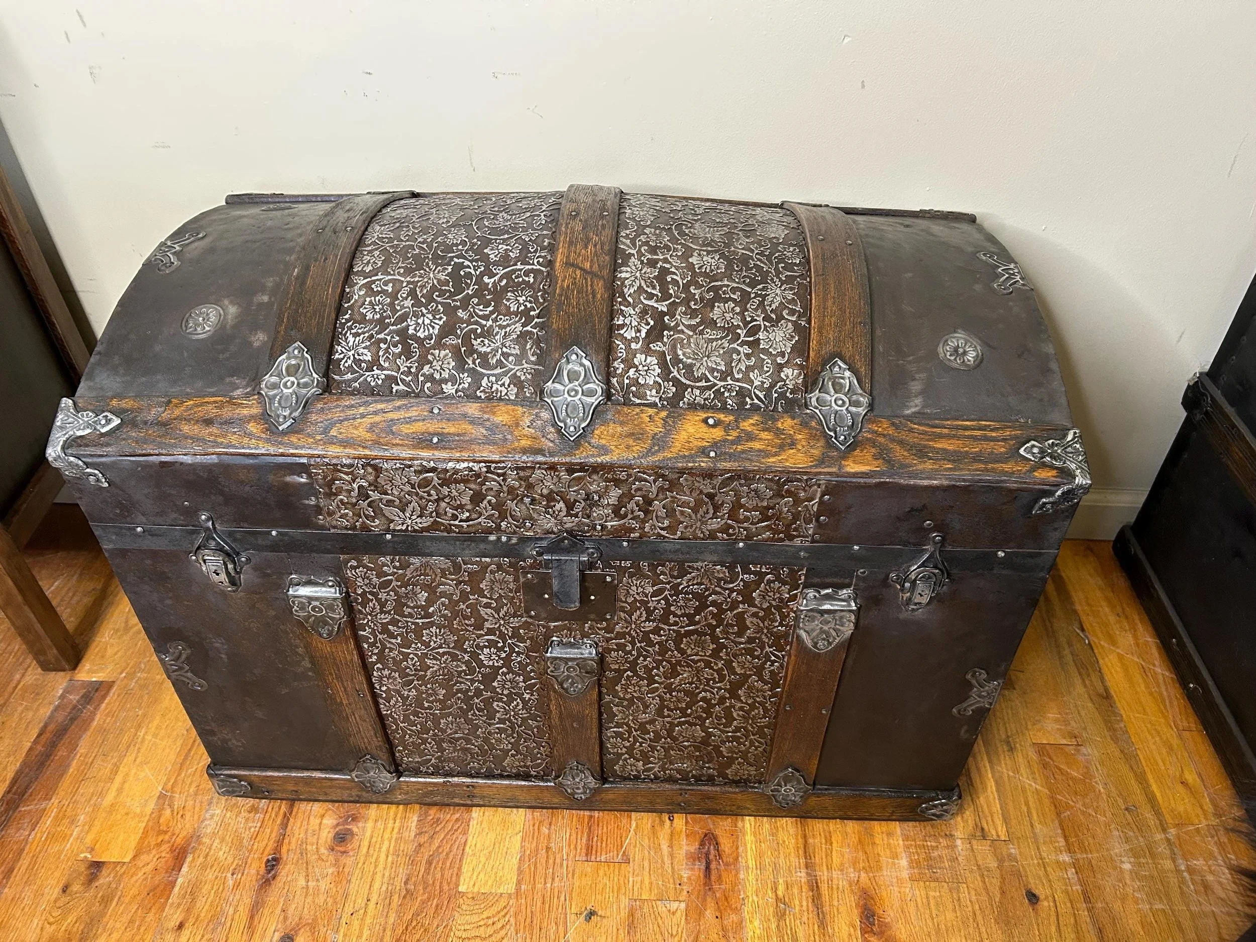 Masterfully restored antique dome top trunk with floral embossed tin and walnut slats.
