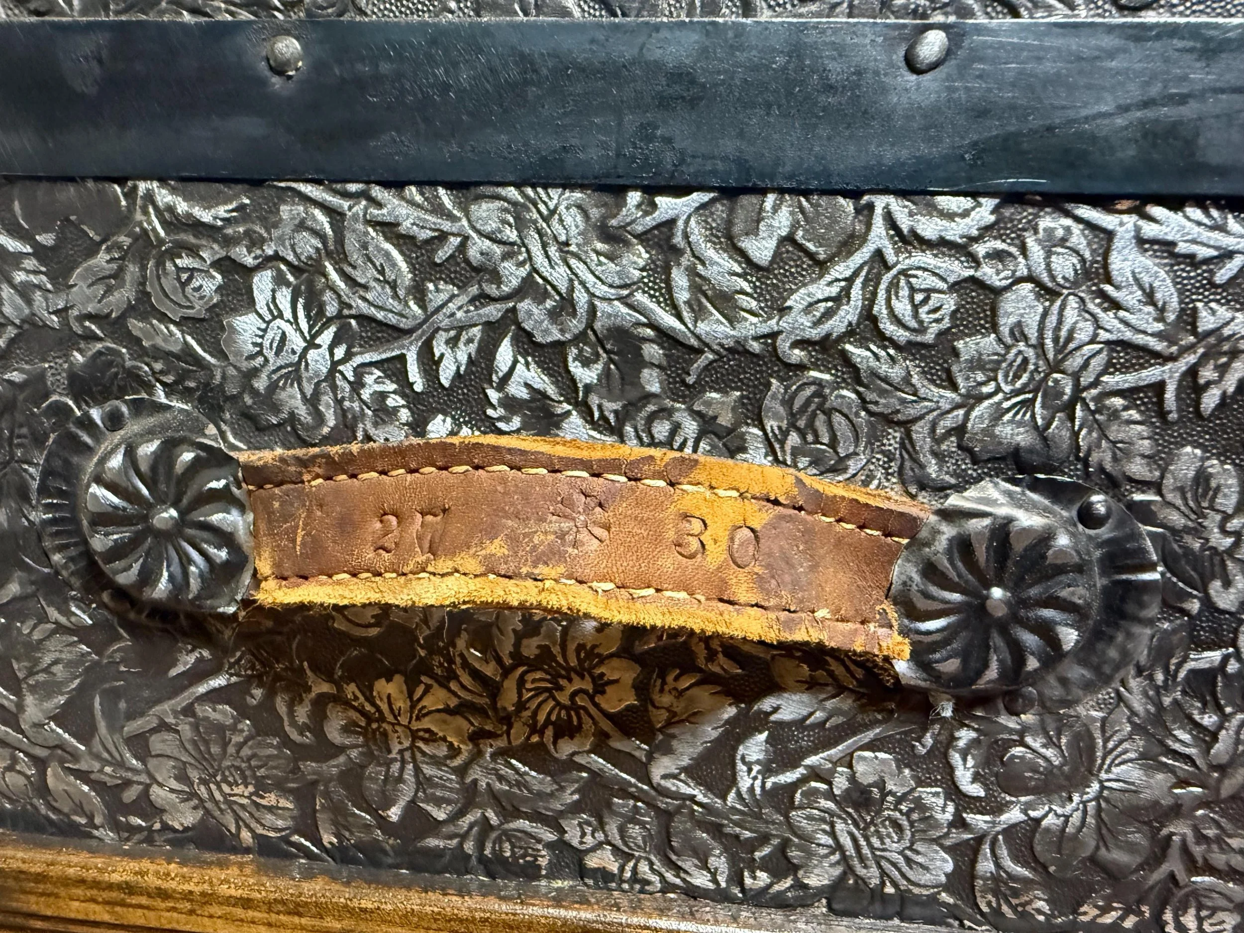 Detailed view of buffed bright floral tin blossoms on an antique dome top steamer trunk with original handles