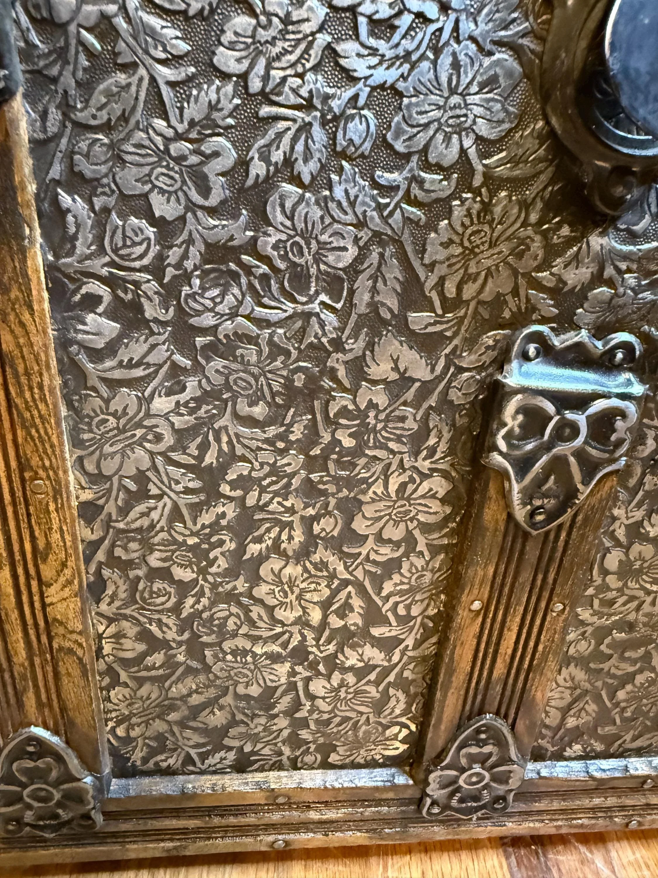 Brilliant contrast between the hand-buffed floral metal relief and the deep walnut-stained oak wood slats on a restored dome top trunk.