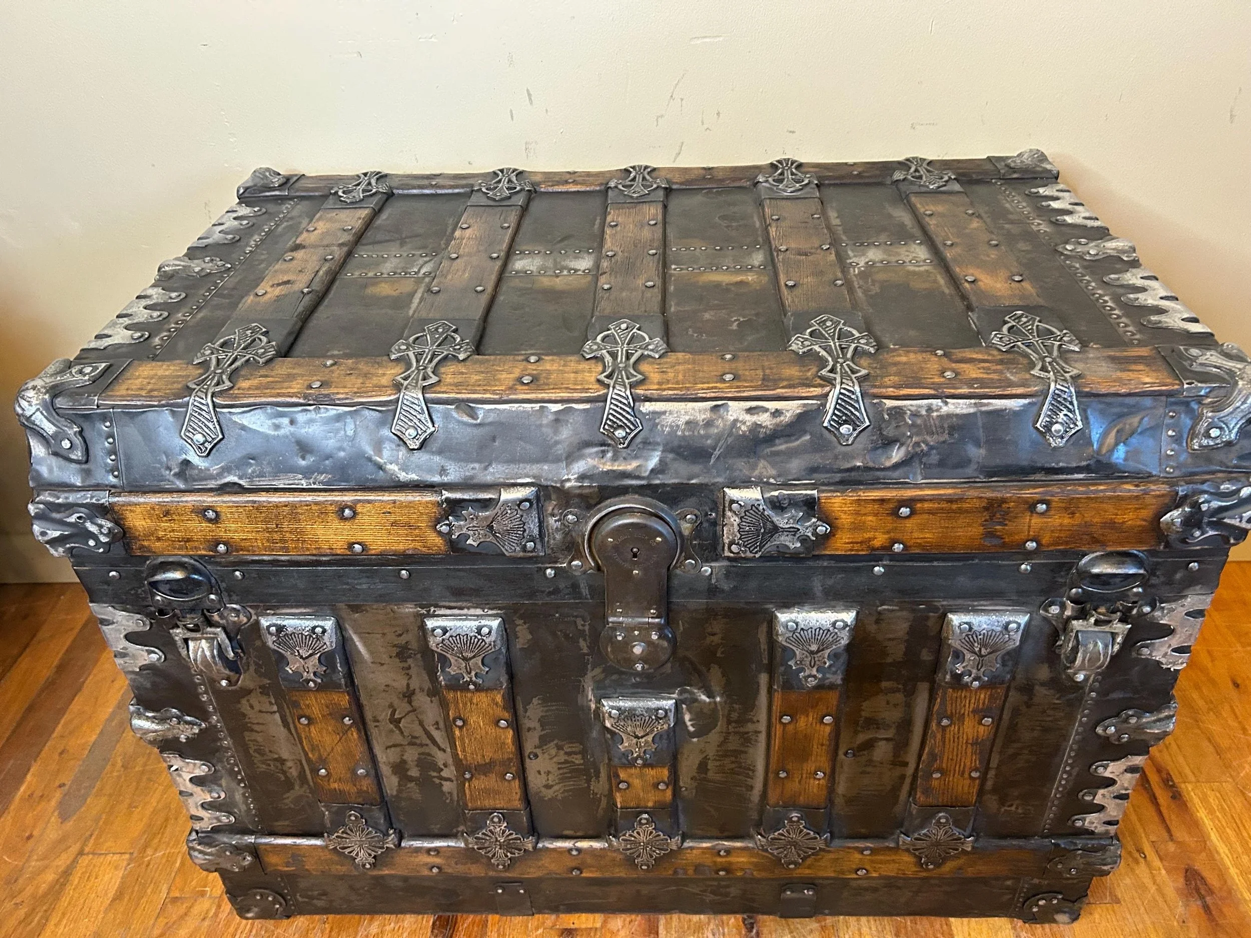 Antique flat top trunk with excessively ornate metal hardware and aged black finish