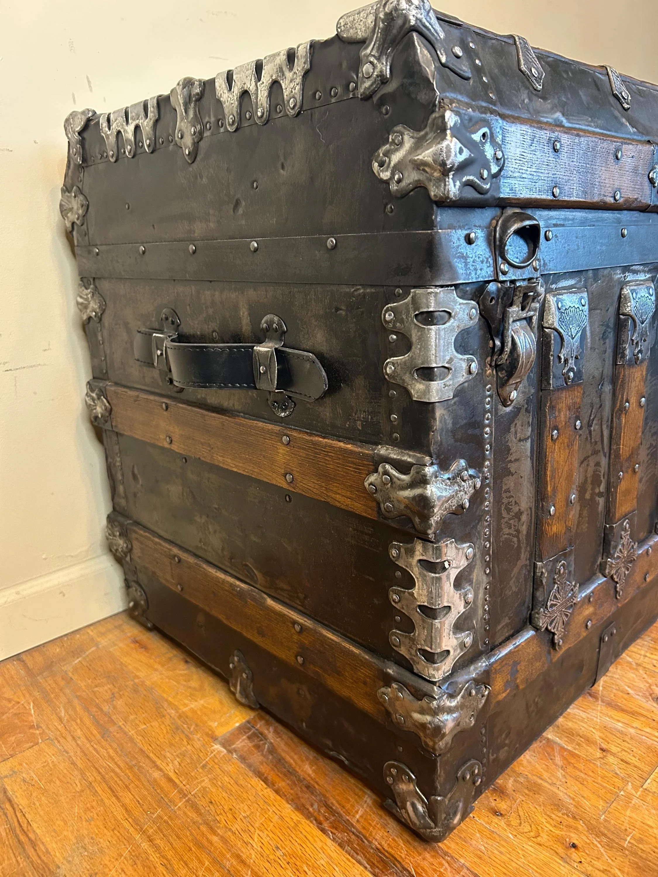 Side profile of a flat tin steamer trunk with a rich hand-applied black patina.