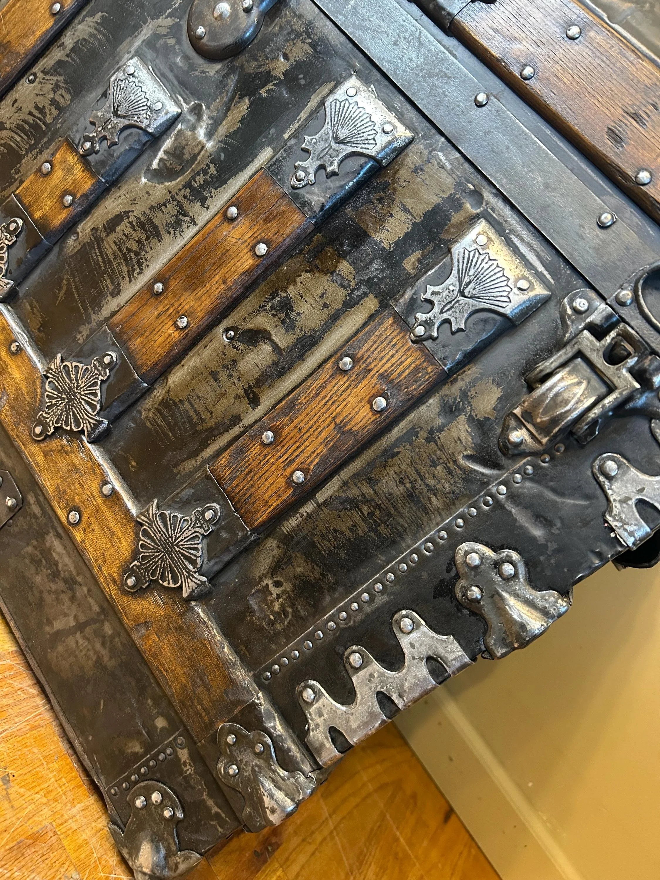 Close-up of the intricate ornate Victorian metal hasps on an aged black chest.