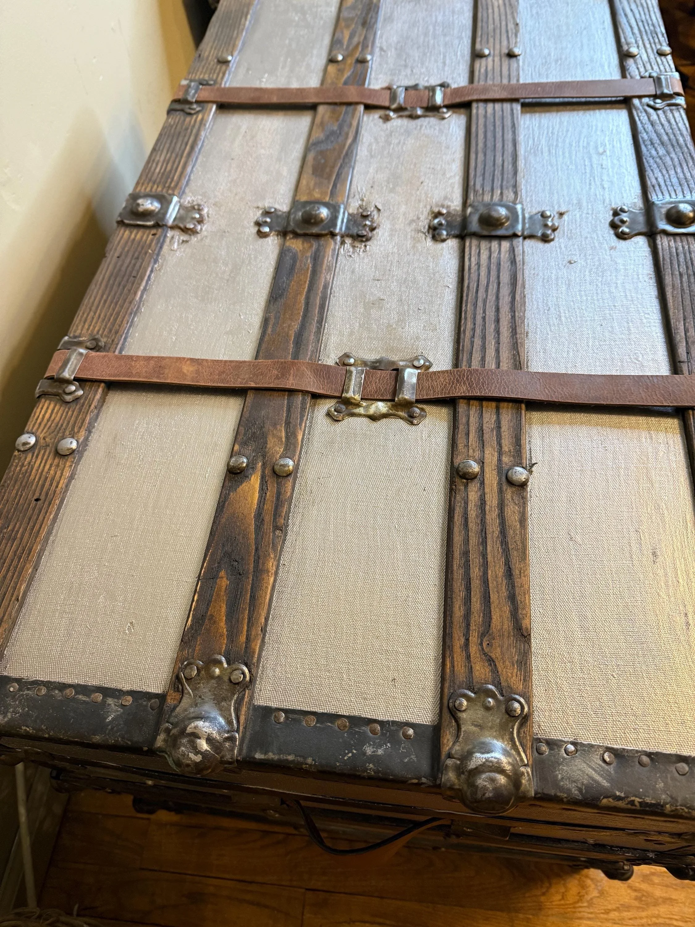 Detailed close-up of original leather straps and metal buckles on a silver metallic antique trunk