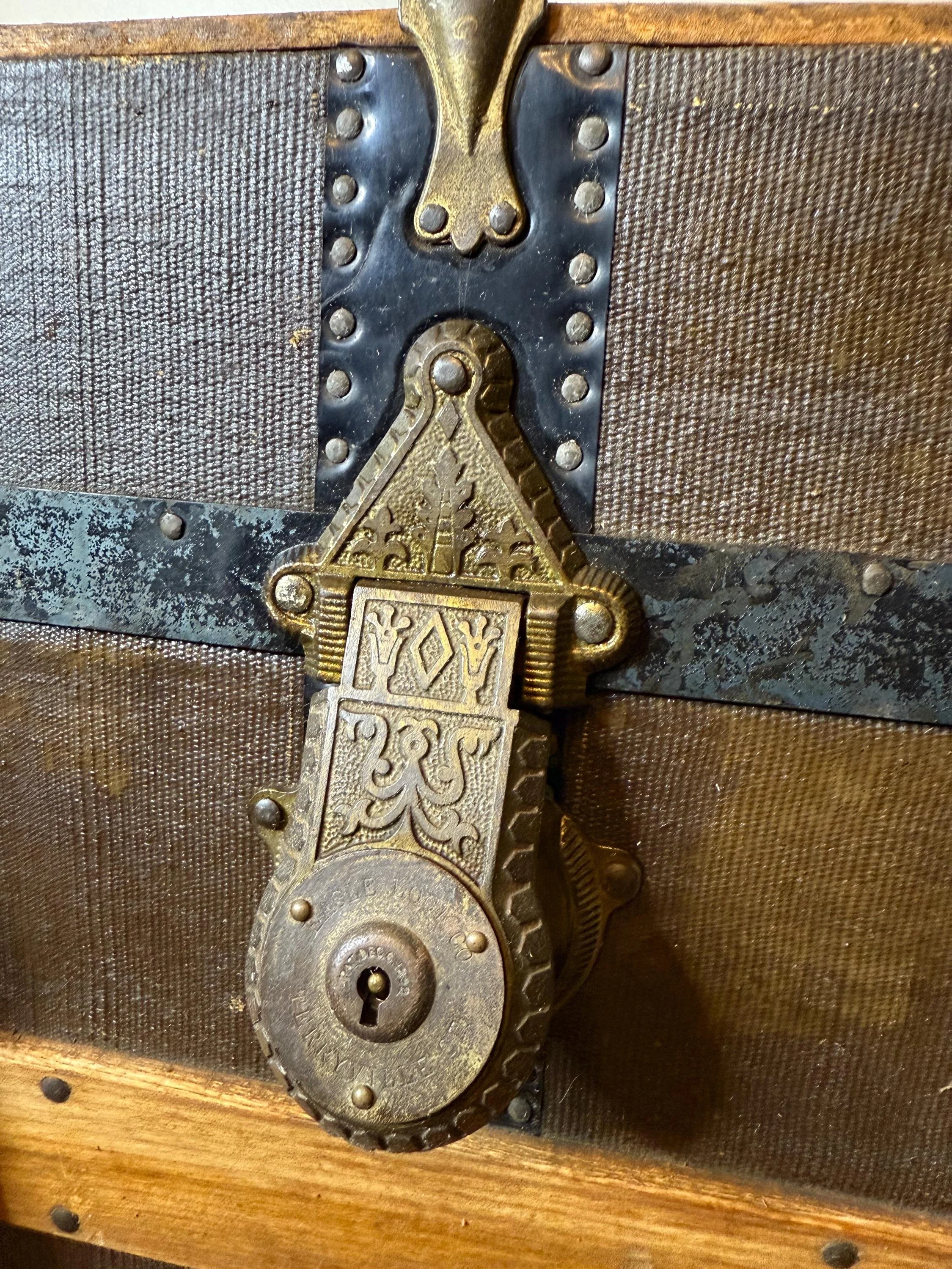 Detailed view of the unusually ornate metal center hasp and brass hardware on a vintage chest.