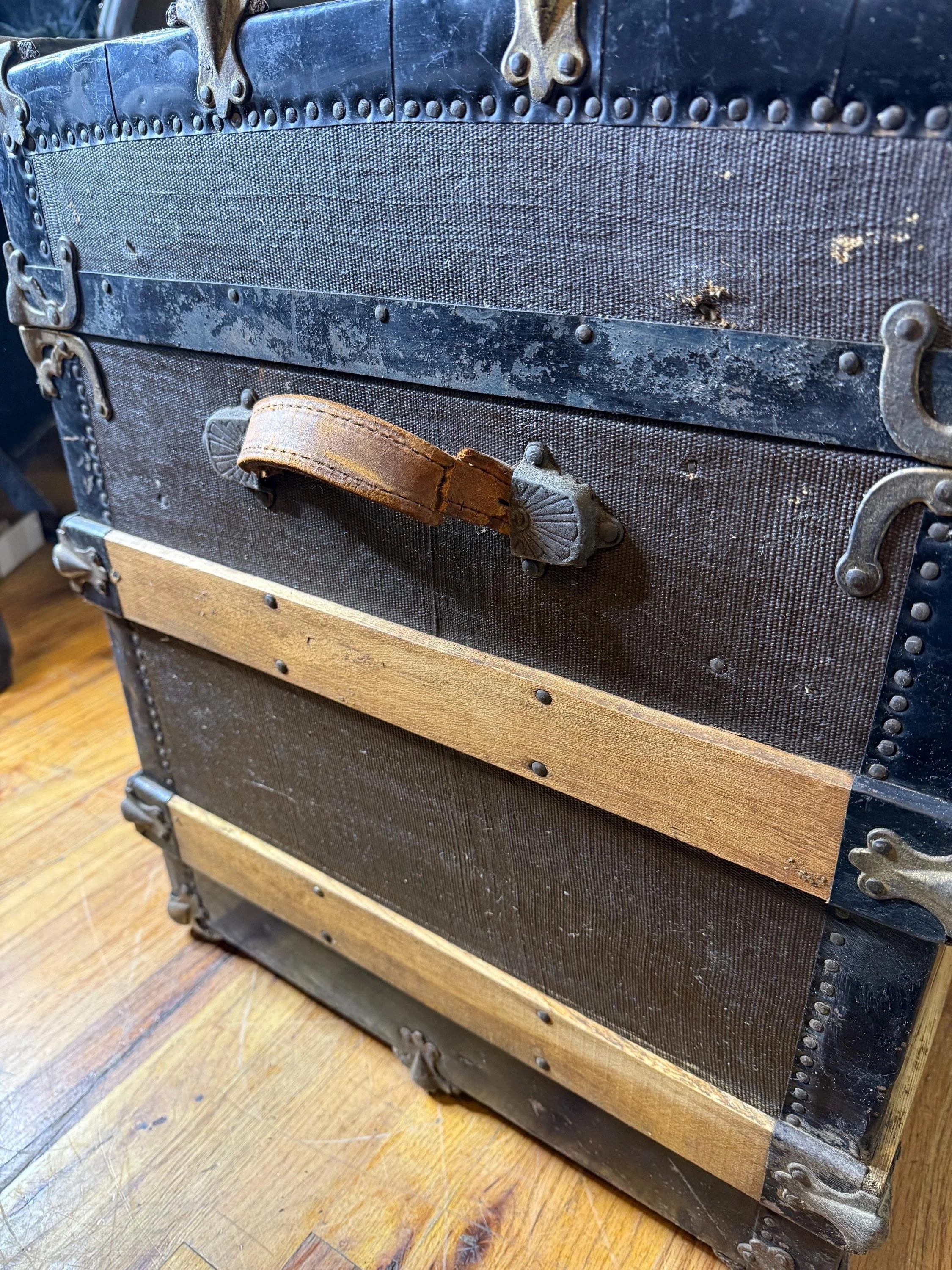Close-up of natural oak slats and original leather straps on a vintage luggage chest.