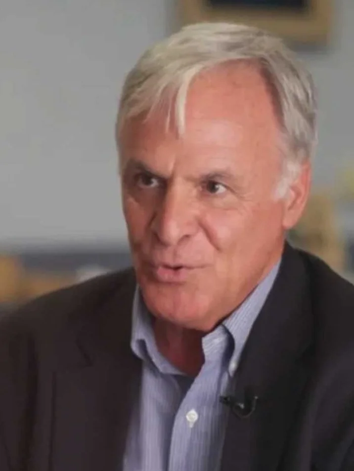 A man with gray hair and a blazer, talking during an interview or discussion.