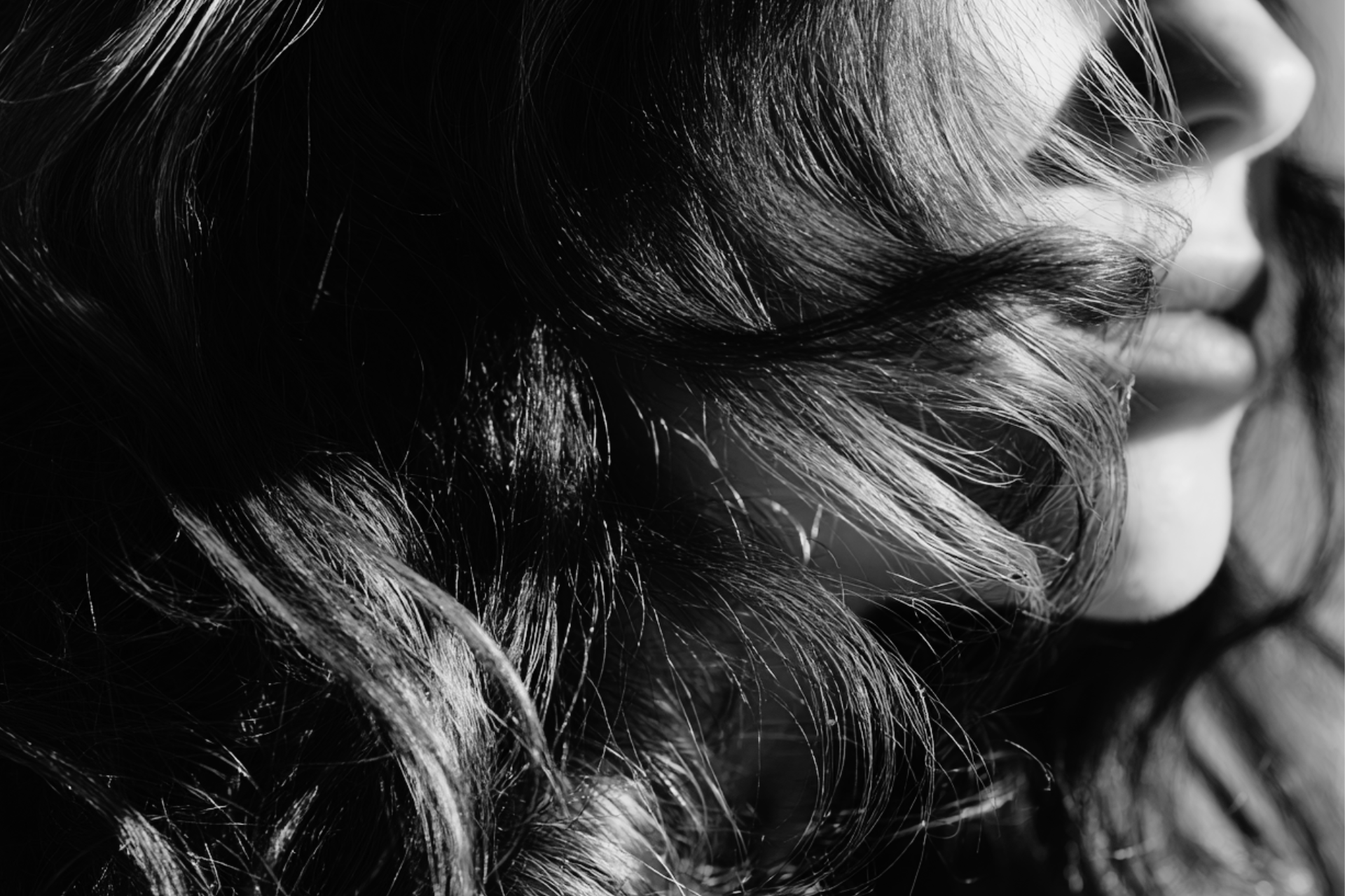 Close-up black and white photo of wavy, shiny hair and lips.