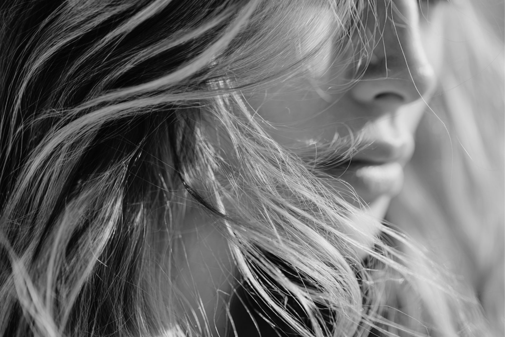 Close-up of a woman's face with long hair partially covering her face, in black and white.
