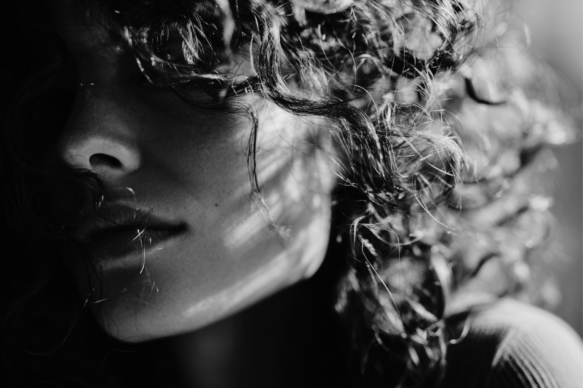 Close-up black and white photo of a woman's face with curly hair partially covering it.