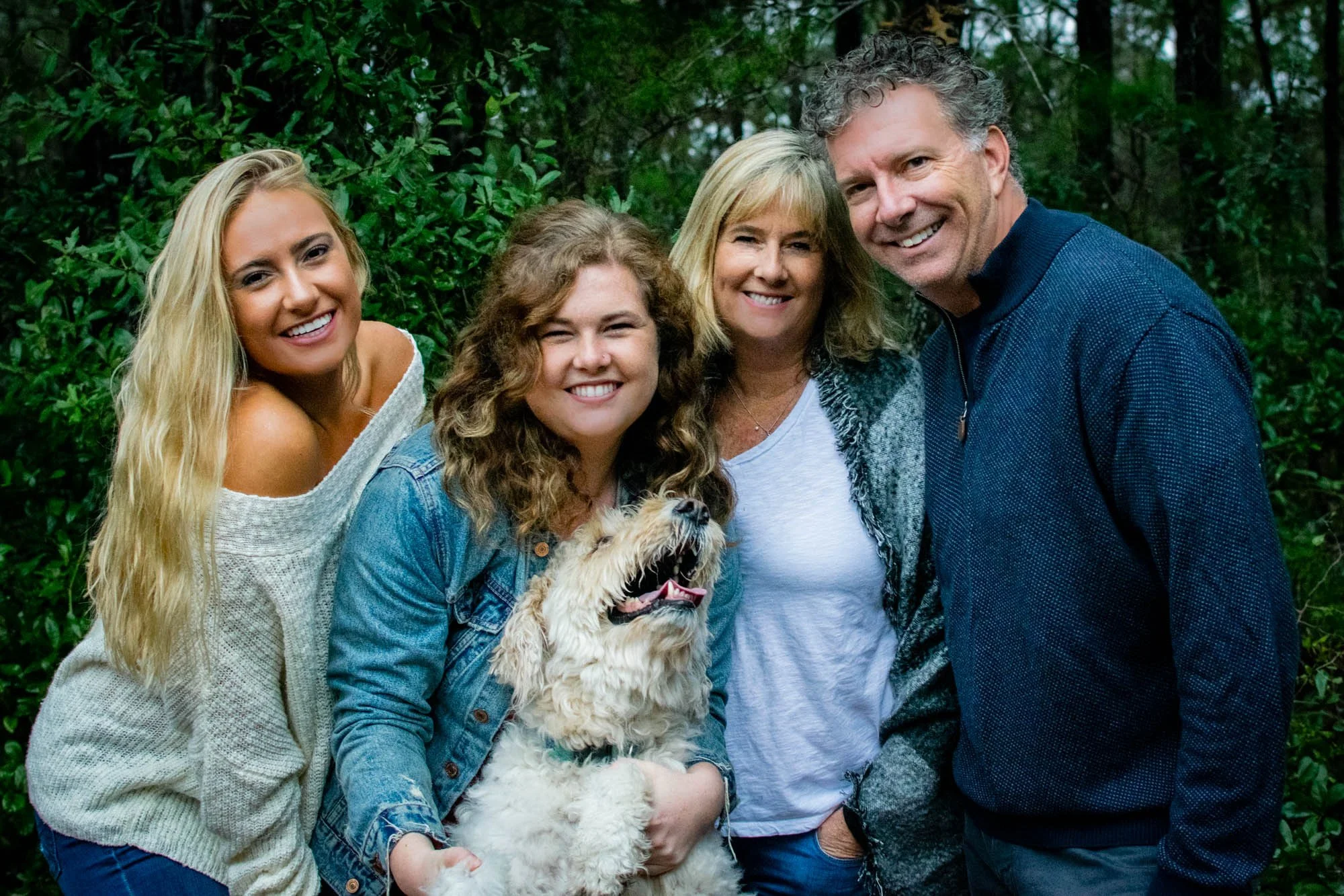 Group of three women and a man with a dog outdoors near greenery, smiling at the camera in Nocatee, Florida.