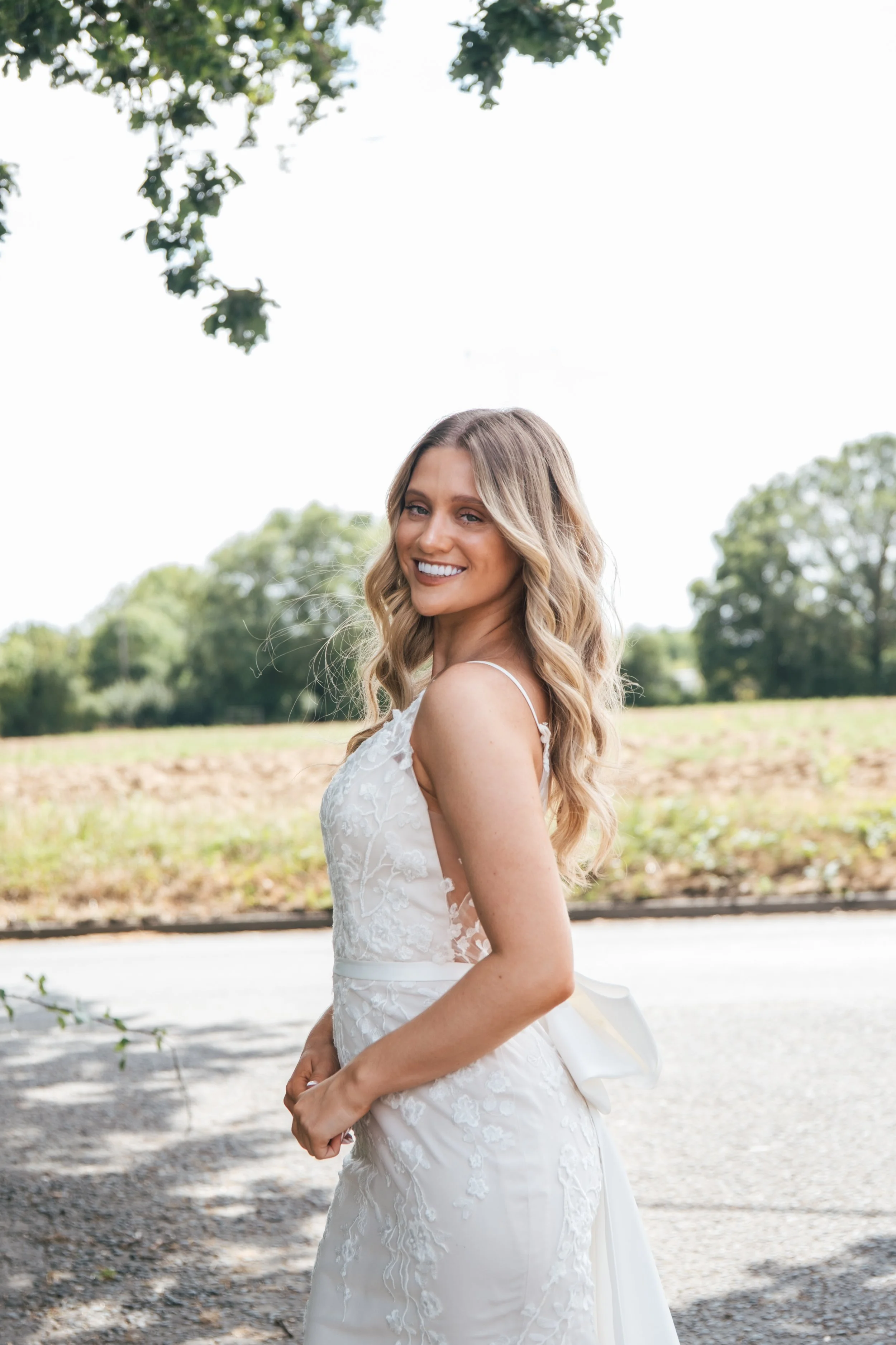 A woman in a white wedding dress smiling outdoors.