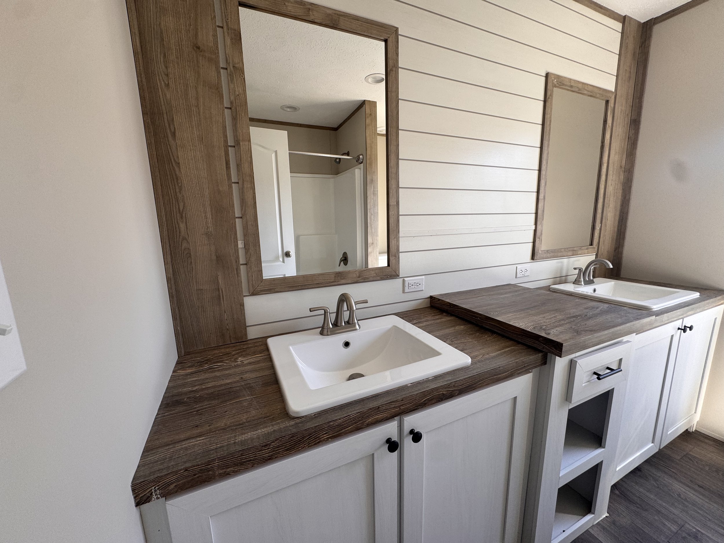 Bathroom vanity with a white sink, a wooden countertop, a large mirror, white cabinets with black handles, and a shiplap-style wall.