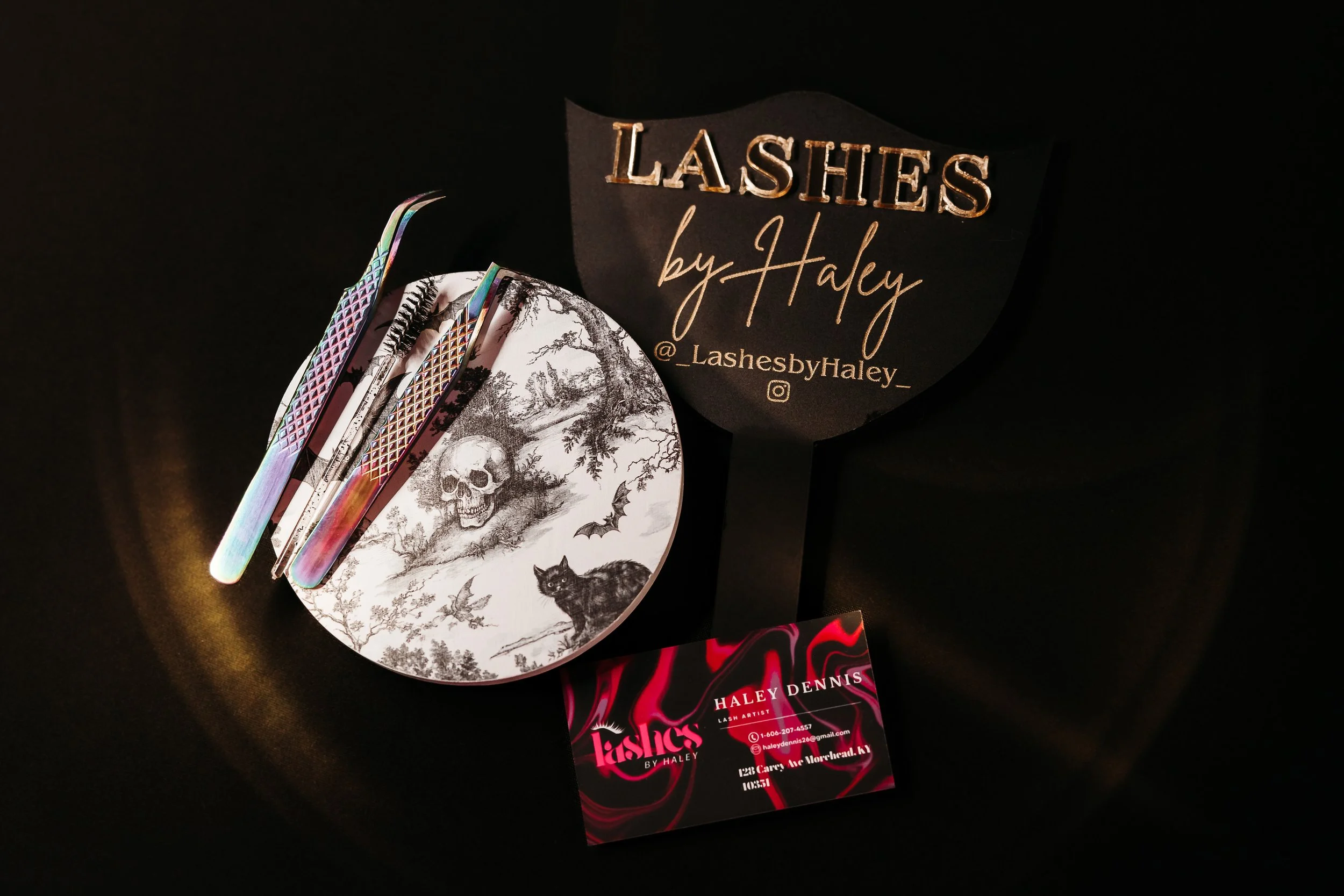 A display of eyelash extensions and tools on a table, with a sign that says "LASHES by Haley @_LashesbyHaley_" and a business card for Haley Dennis, a lash artist.