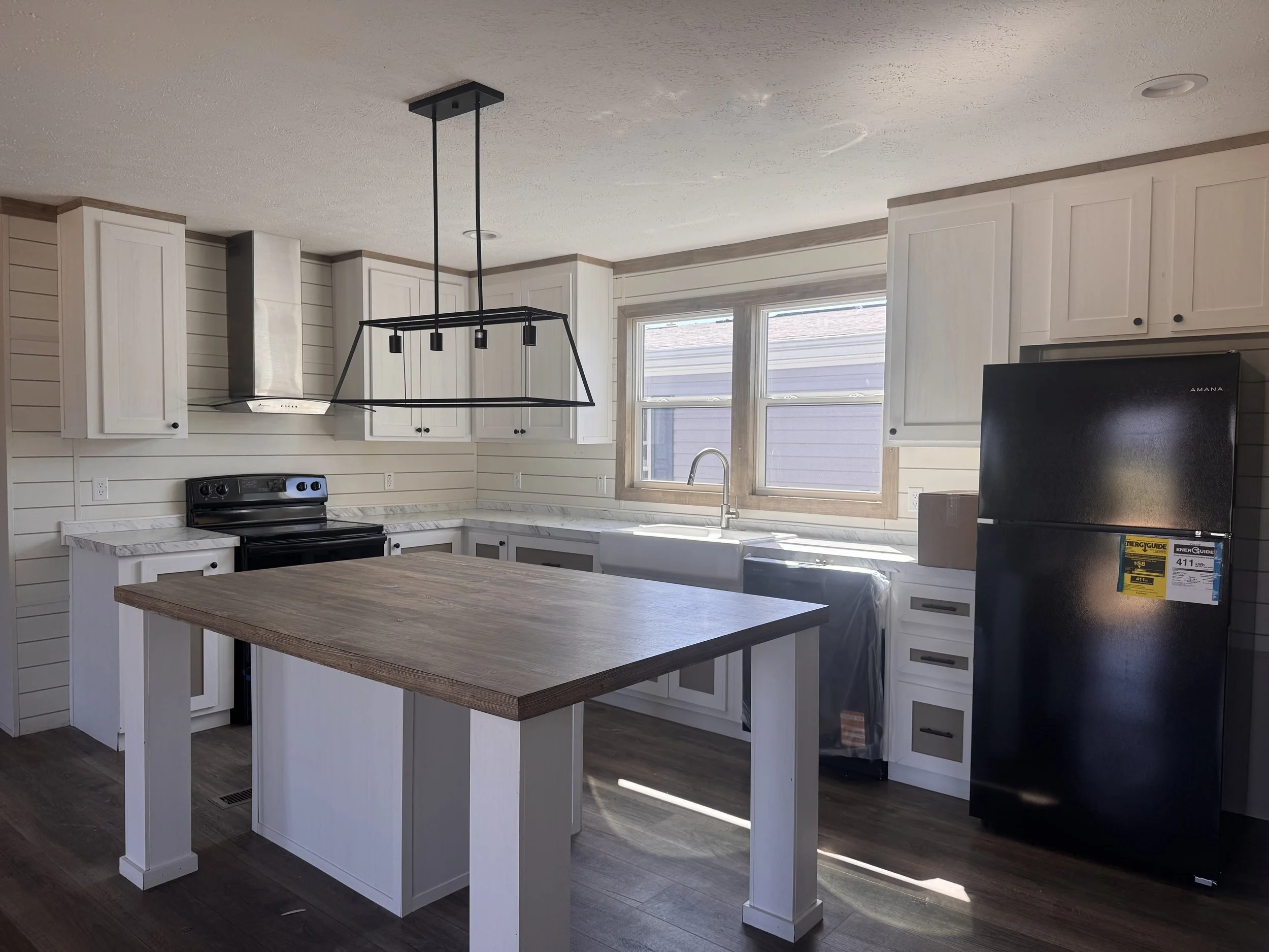 Kitchen with white cabinets, black appliances, a large wooden kitchen island, and modern black pendant lighting.