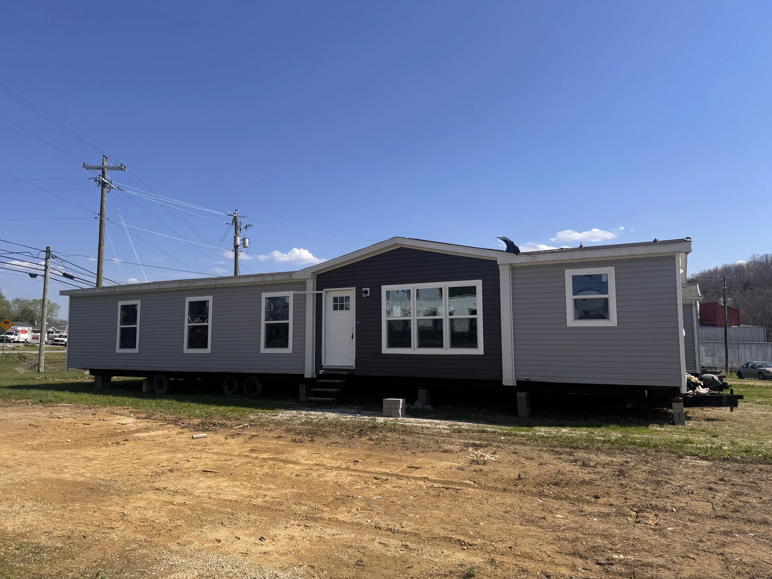 A gray modern house with multiple windows and a white door, under a clear blue sky with some clouds, and power lines.