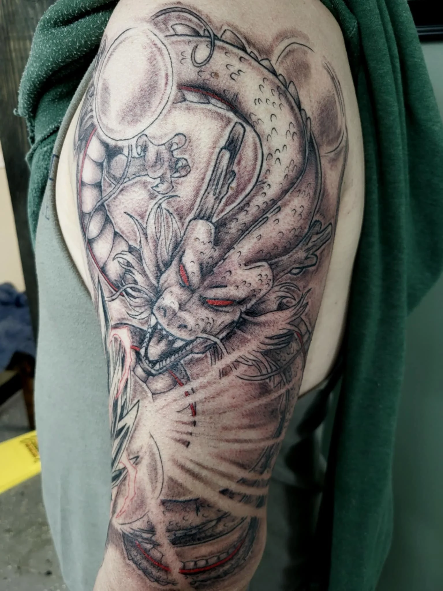 Tattoo of a fierce dragon's head on a person's upper arm, detailed in black and gray ink with some red accents.