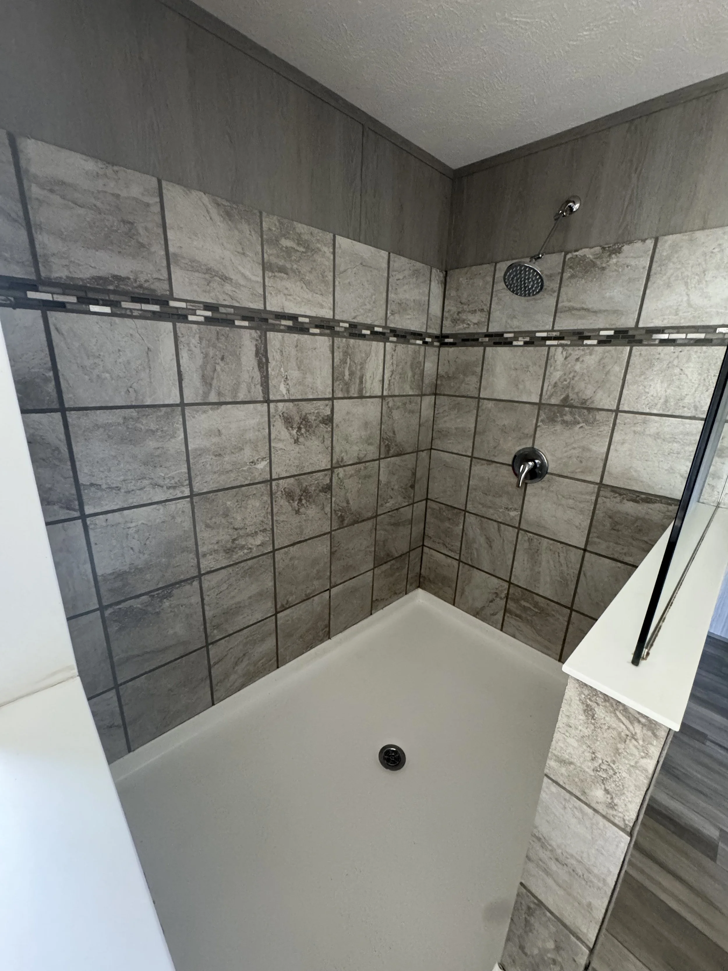 Showers with beige and gray tiles, a rain shower head, and a handheld shower head, with a white shower base and silver fixtures.