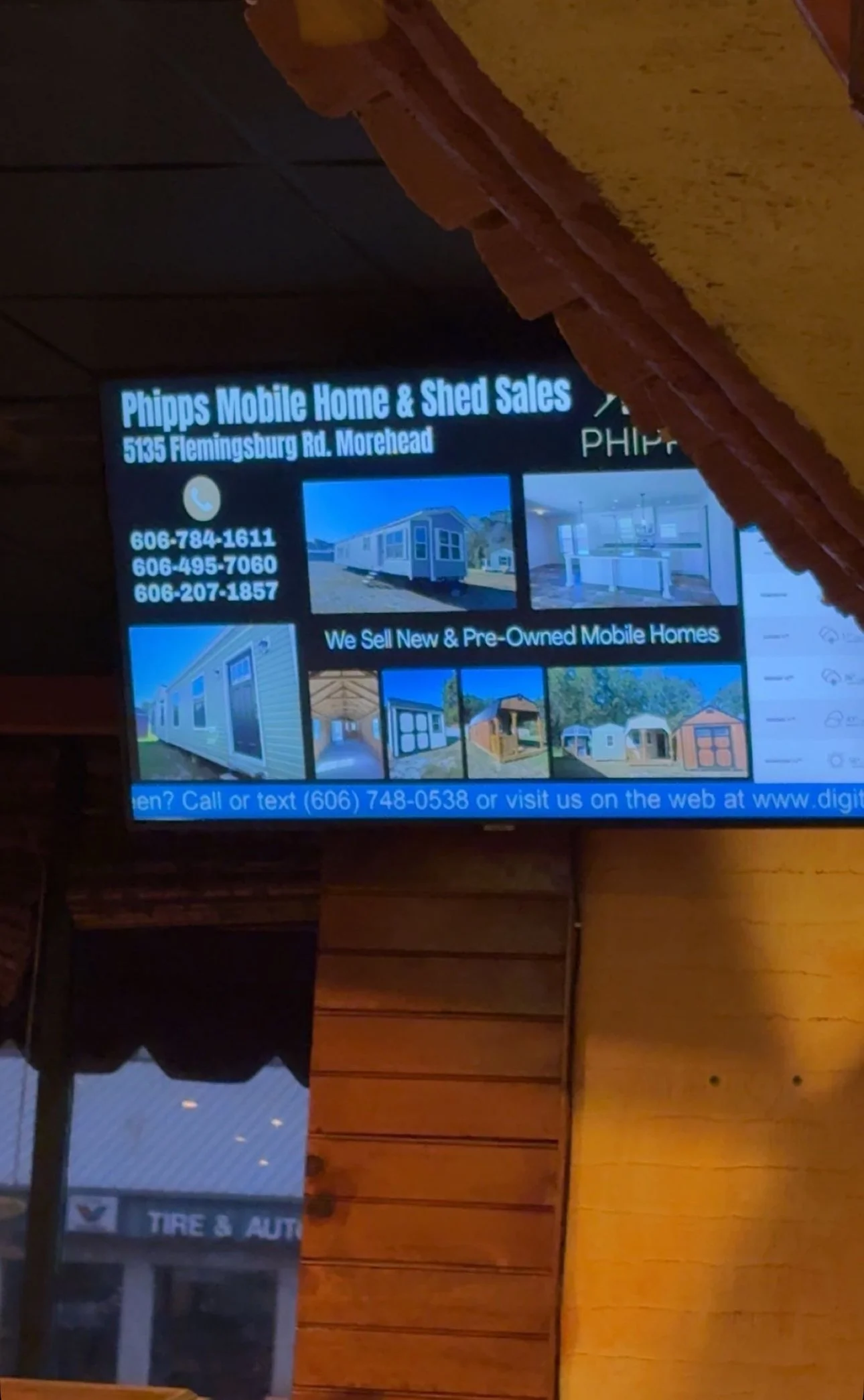 Digital screen advertisement for Phipps Mobile Home & Shed Sales, located at 5135 Flemingsburg Rd. Morehead. It shows images of mobile homes, sheds, and contact information including phone numbers and a website.
