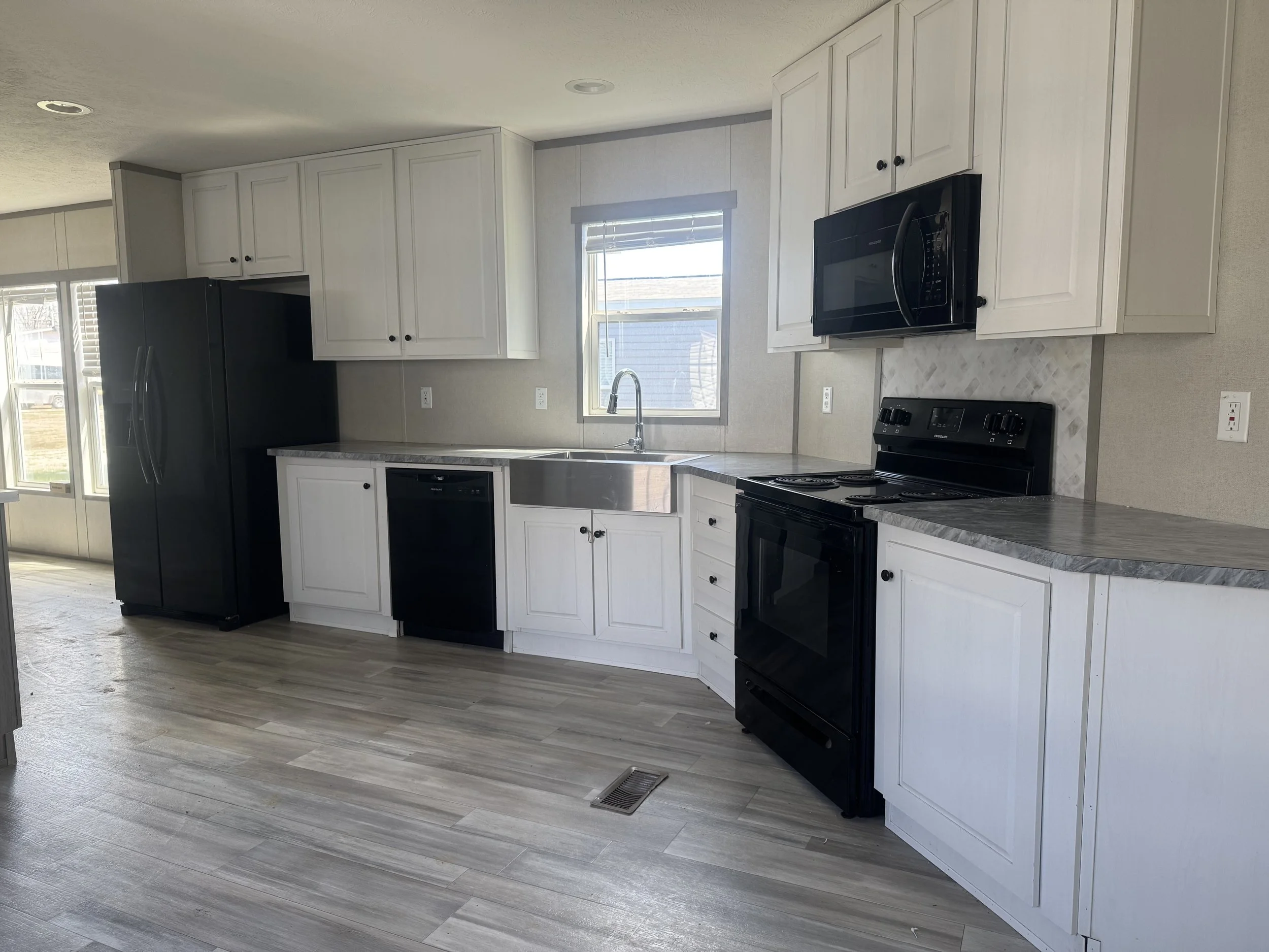 Modern kitchen with white cabinets, black appliances, a window above the sink, and wood-like flooring.