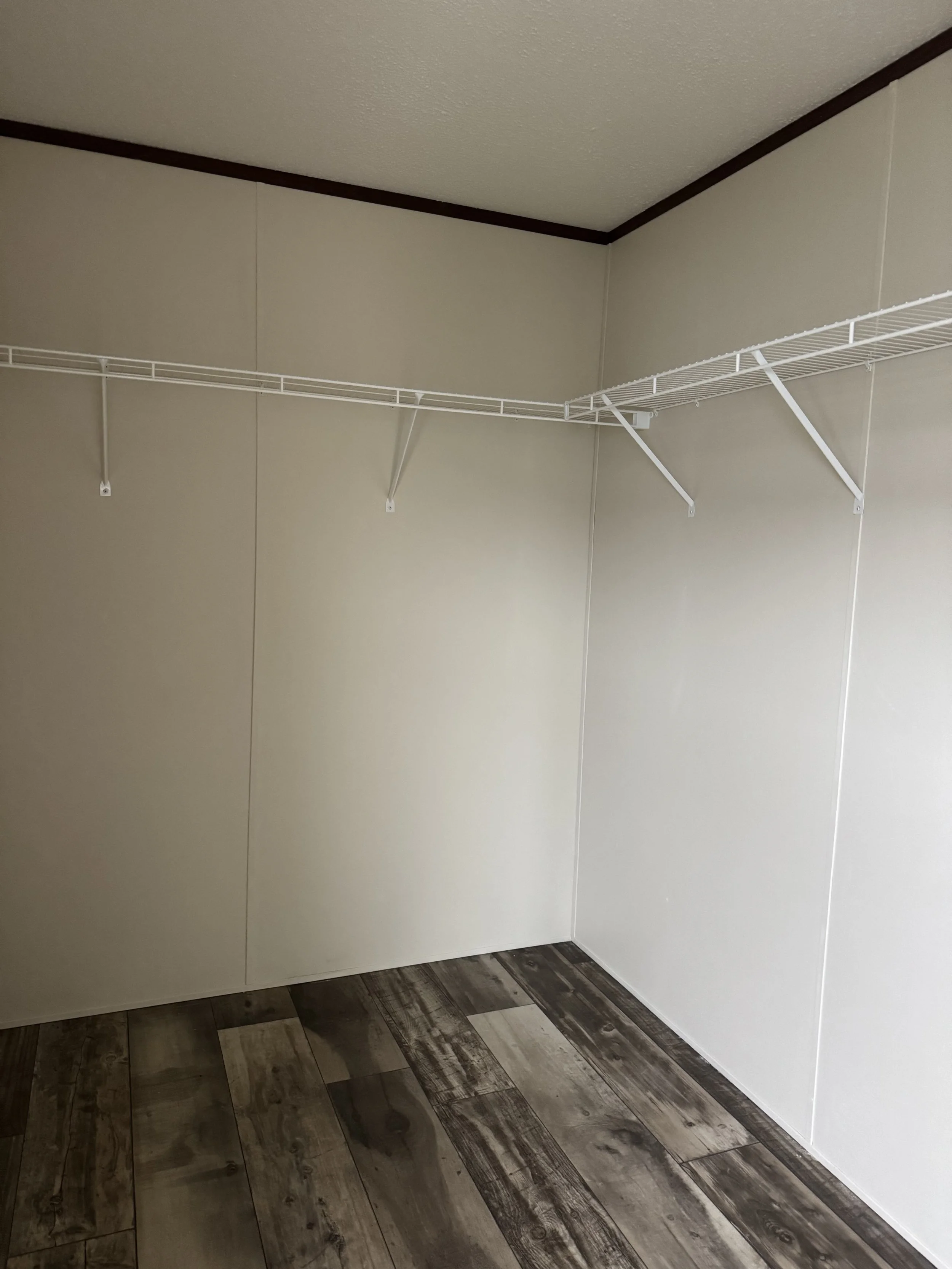 Empty closet with white wire shelf and wood-look vinyl flooring.