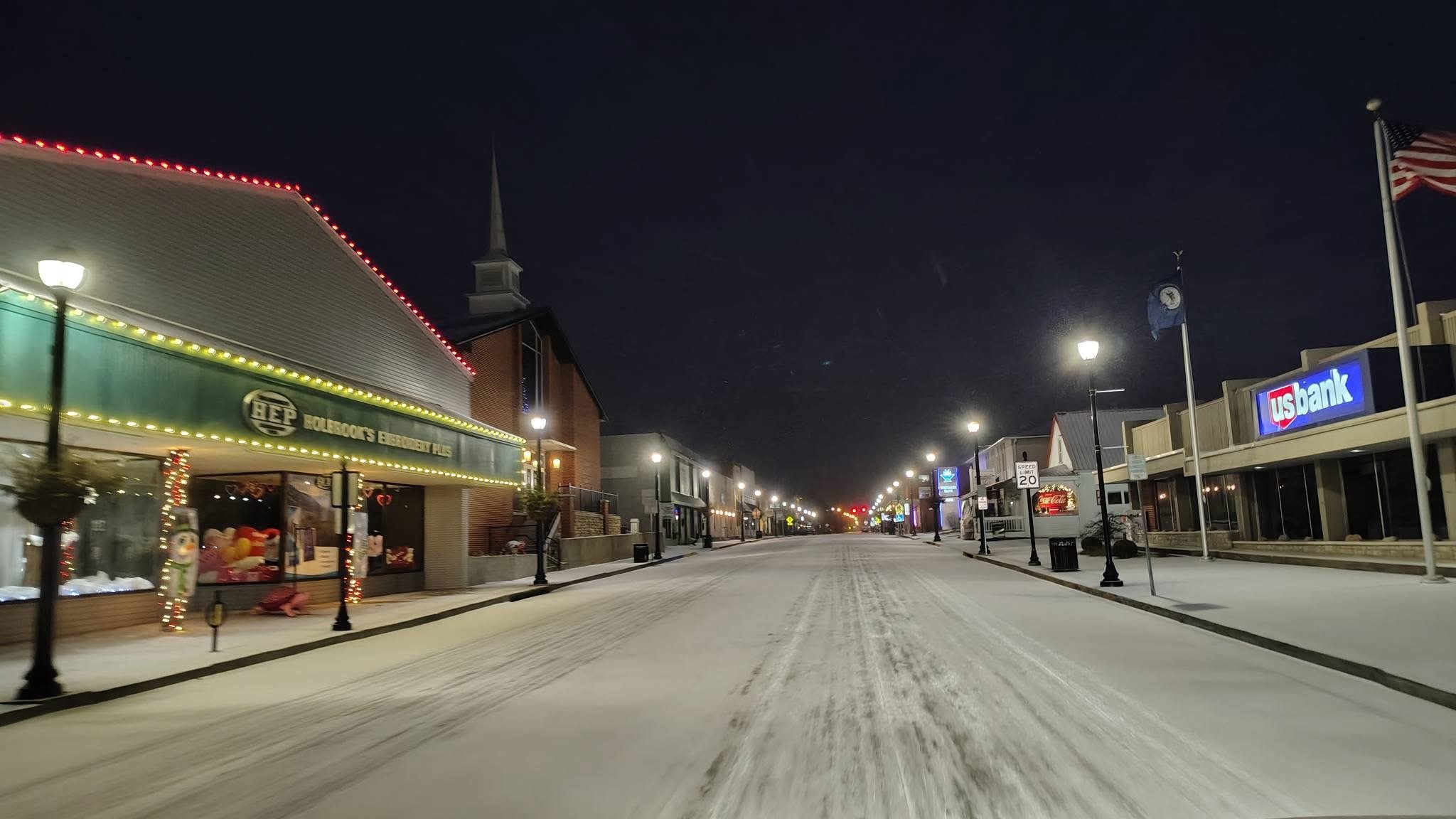 Empty snow-covered Main Street at night with shops and streetlights