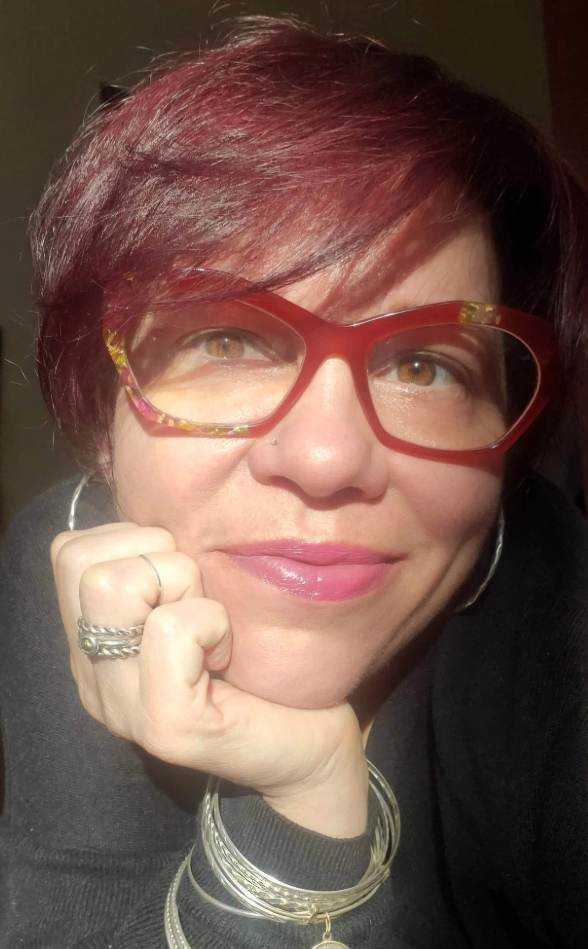 Portrait of Vanessa Quiñones resting her chin on her hand, wearing red glasses and silver bracelets.