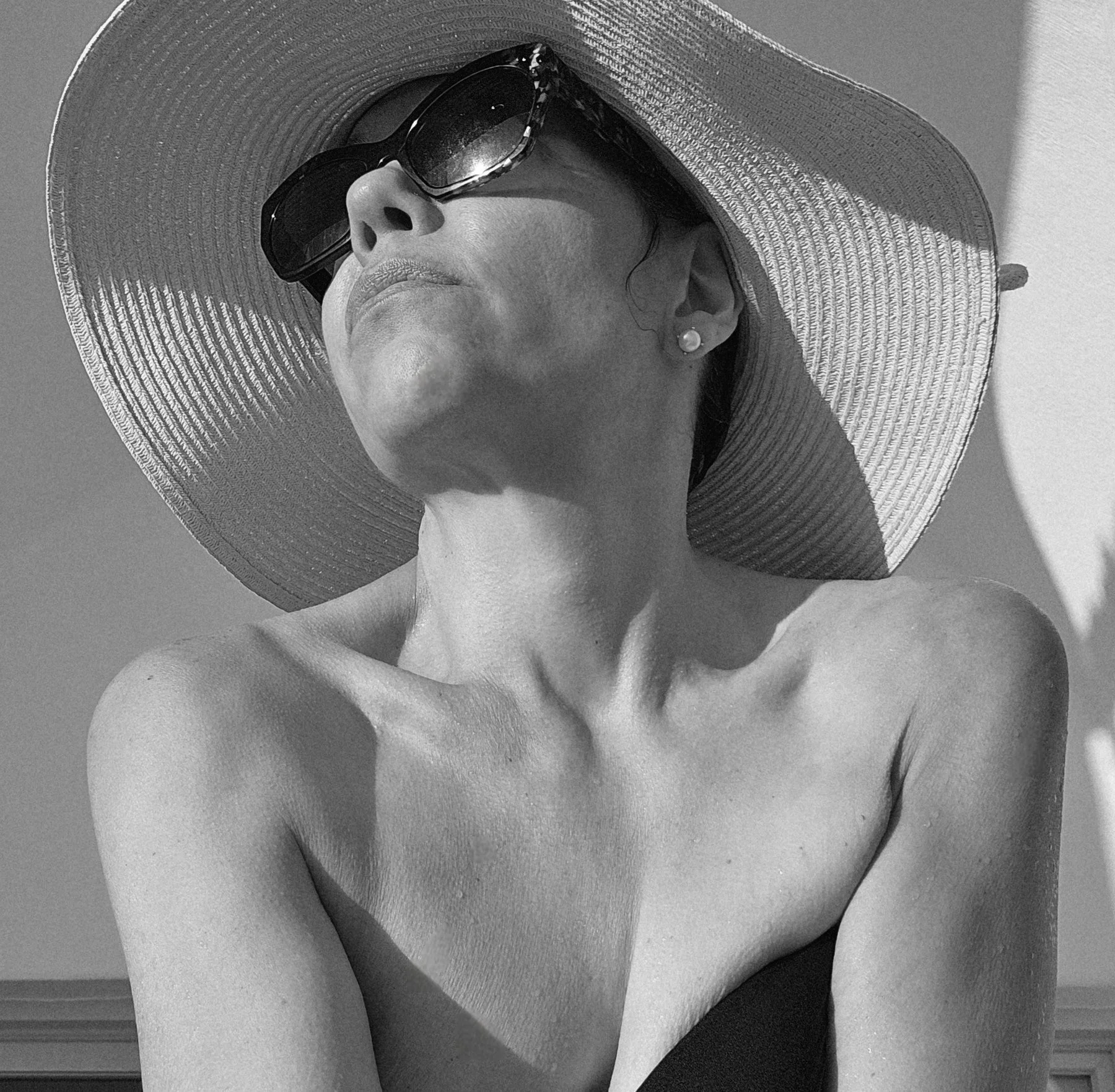 Black-and-white photograph of Vanessa Quiñones in a wide sun hat and sunglasses, her face lifted toward the sun.