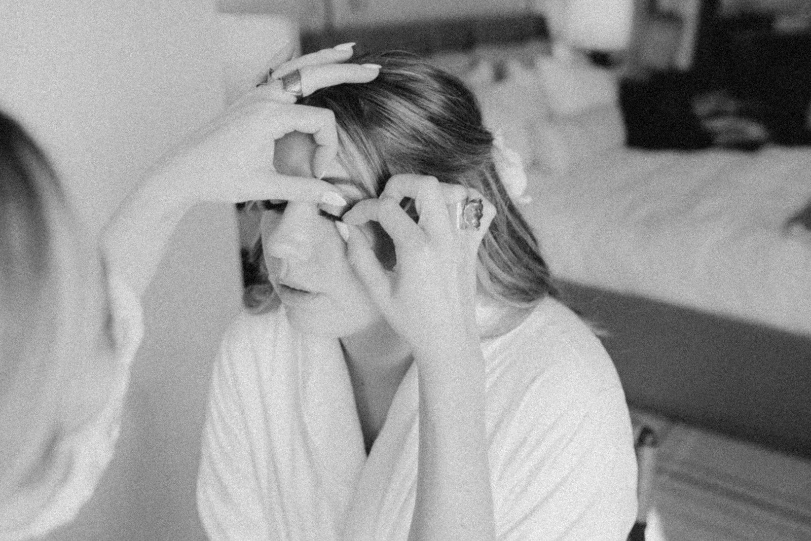 Woman sitting with eye covered by hand, makeup artist applying makeup to her face