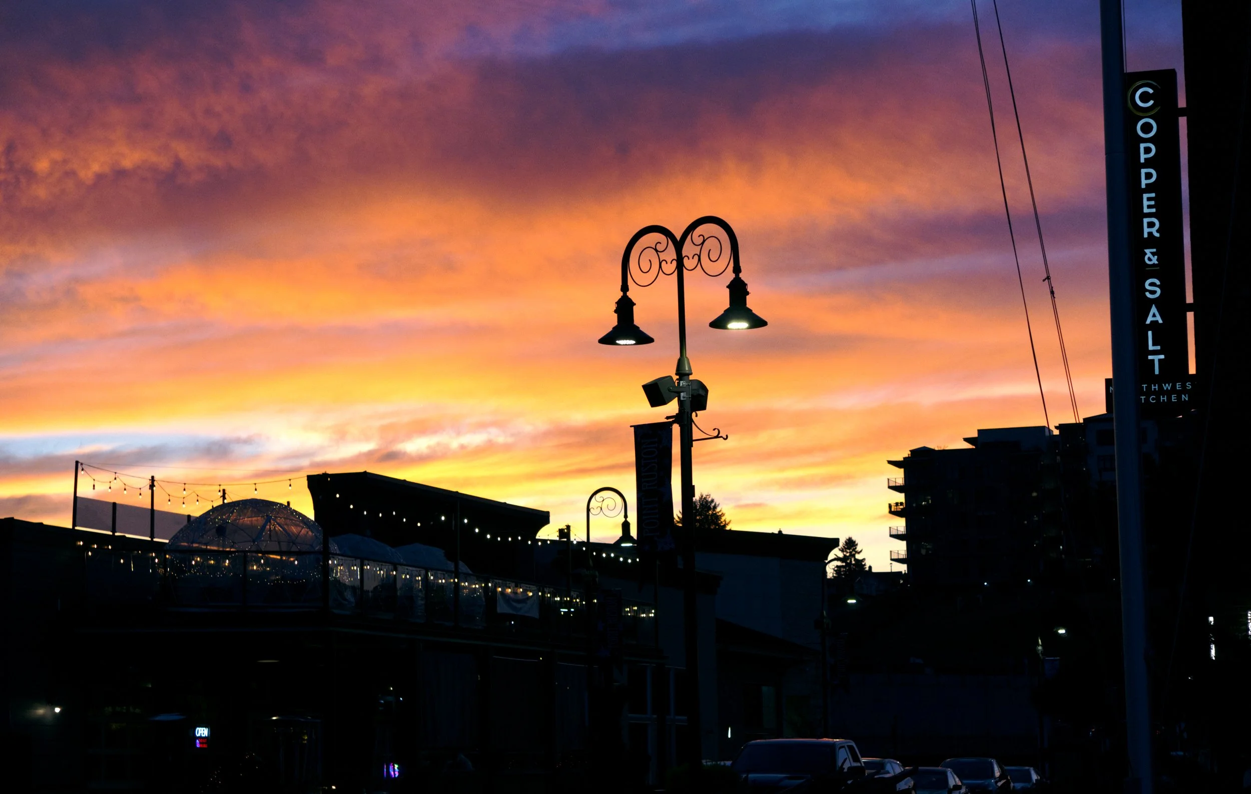 Colorful sunset sky over a city street with street lamps, string lights, and buildings.