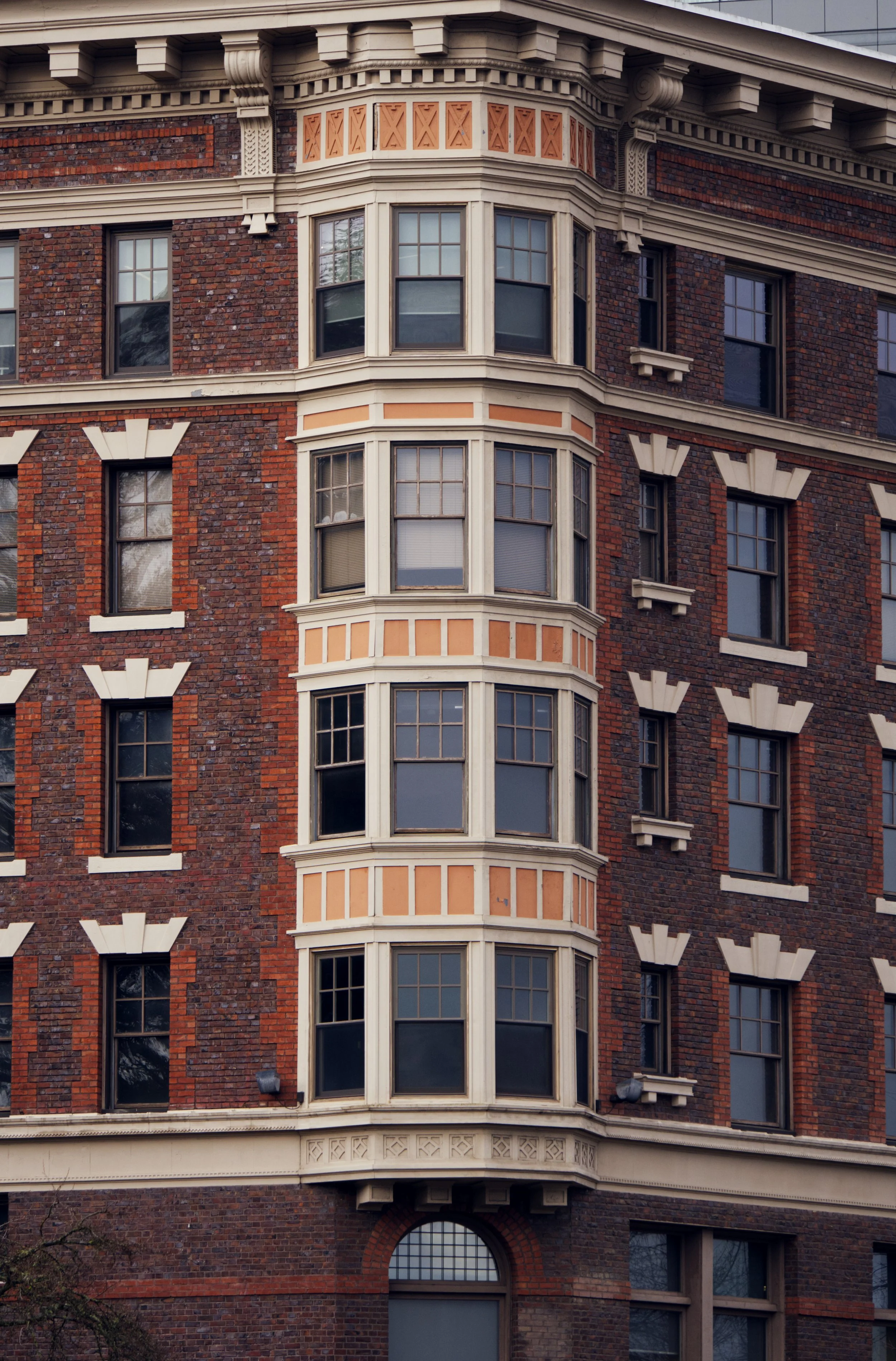 Close-up of a historic red brick building with a rounded bay window featuring multiple smaller windows, decorative white trim, and ornate architectural details.