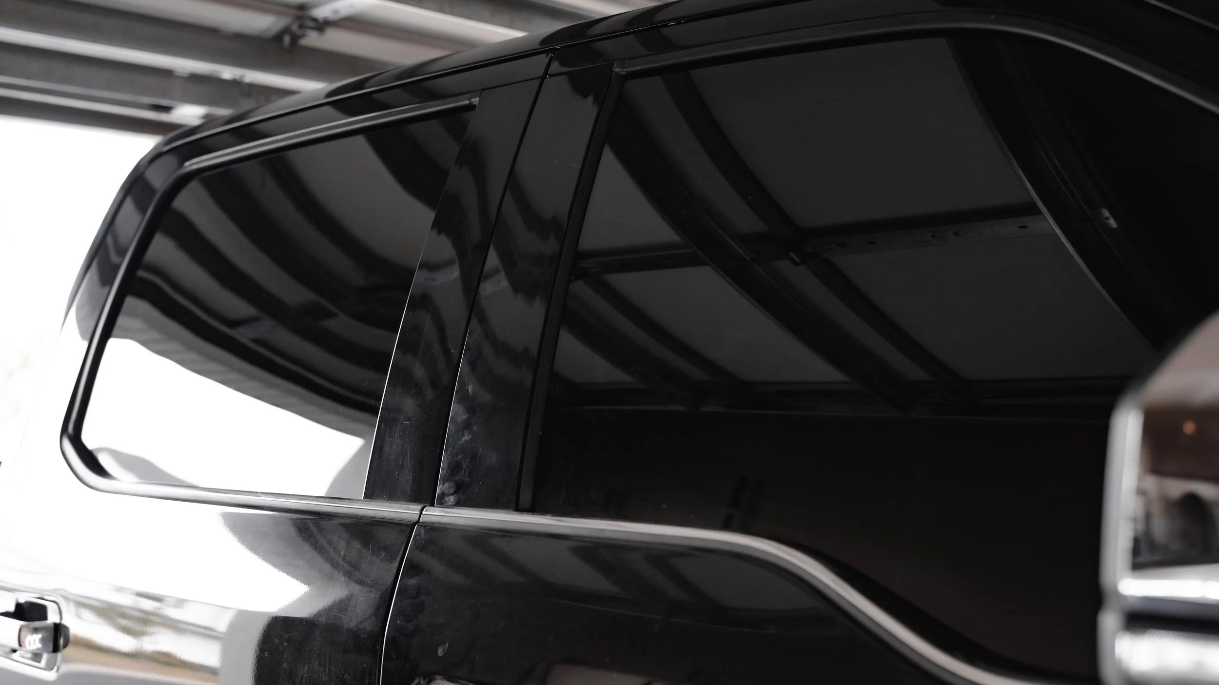 Close-up of a black car with tinted windows parked inside a garage with a metal ceiling.