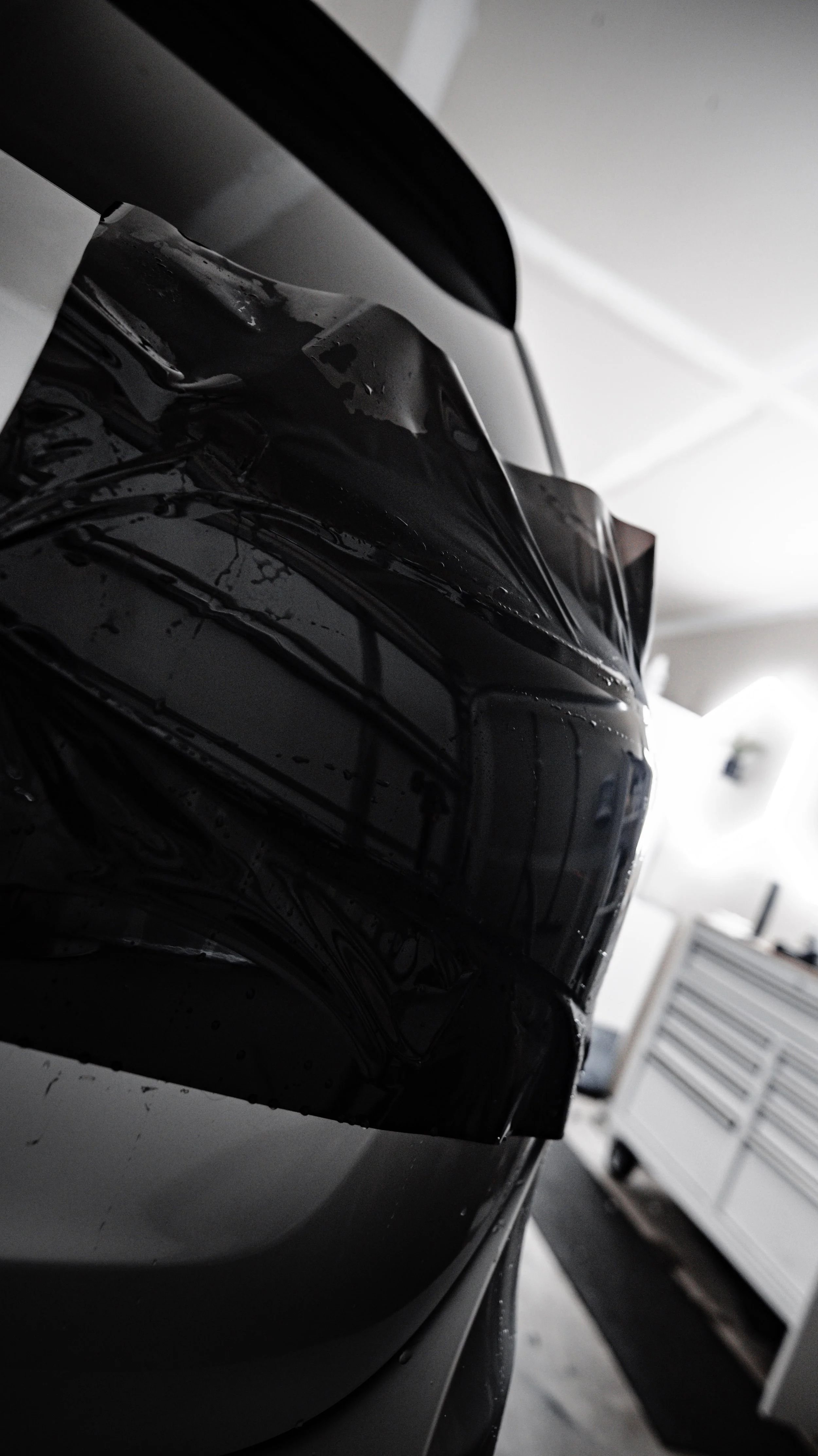 Close-up of a black glossy surface, possibly a car, with a reflection caled a garage or workshop with tool chests in the background.