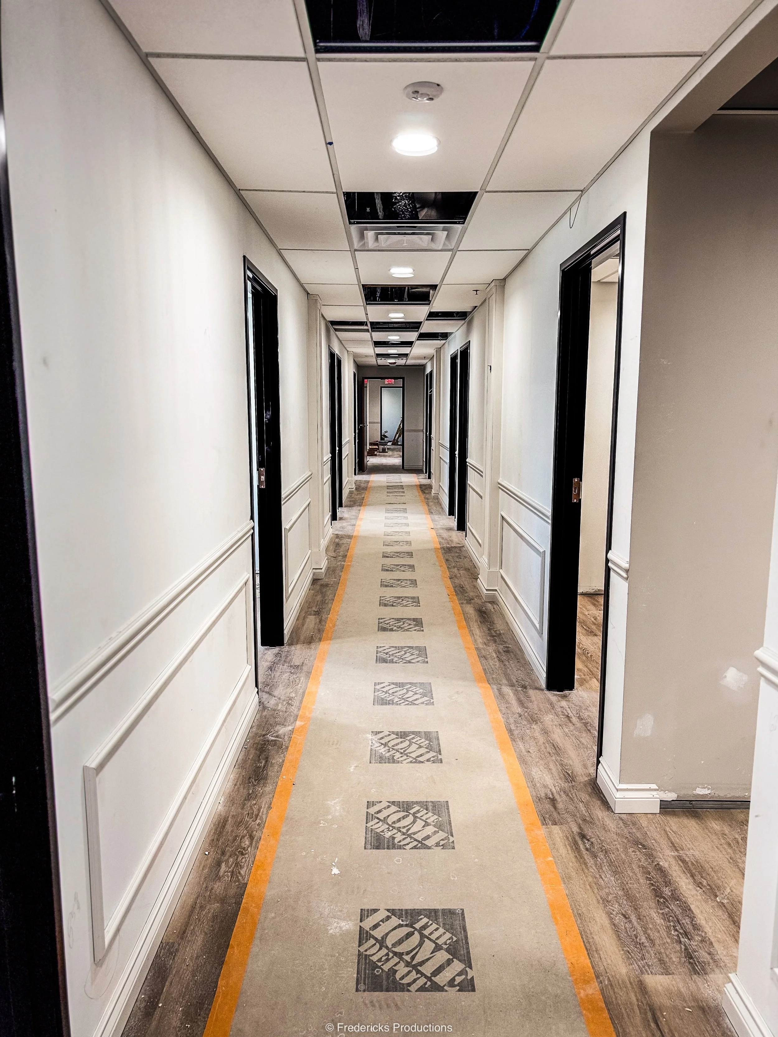 Long hallway in a building under construction or renovation, with walls, doors, and a carpeted floor marked with 'The Home Depot' logo.